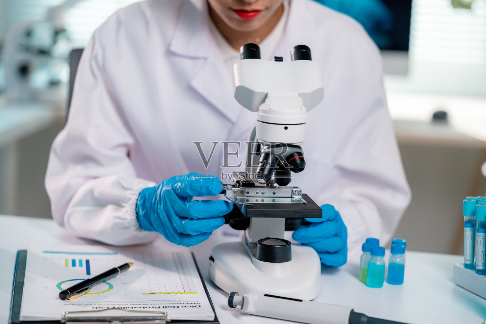 穿着实验室外套和蓝色手套的科学家将玻璃载玻片放置在显微镜上，准备在设备齐全的现代实验室中进行研究和分析。照片摄影图片