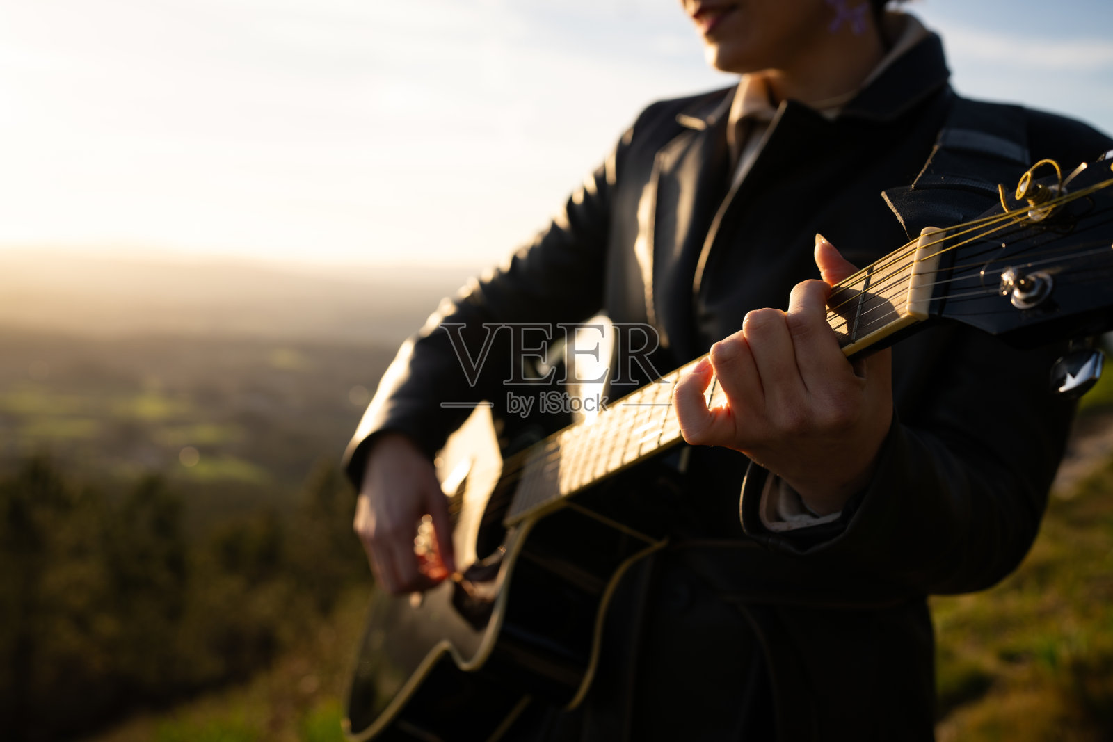 熟练的吉他手在戏剧性的山脉背景下演奏原声旋律，金色的日落光辉照亮了这一音乐时刻，展现了自然之美和艺术表现。照片摄影图片