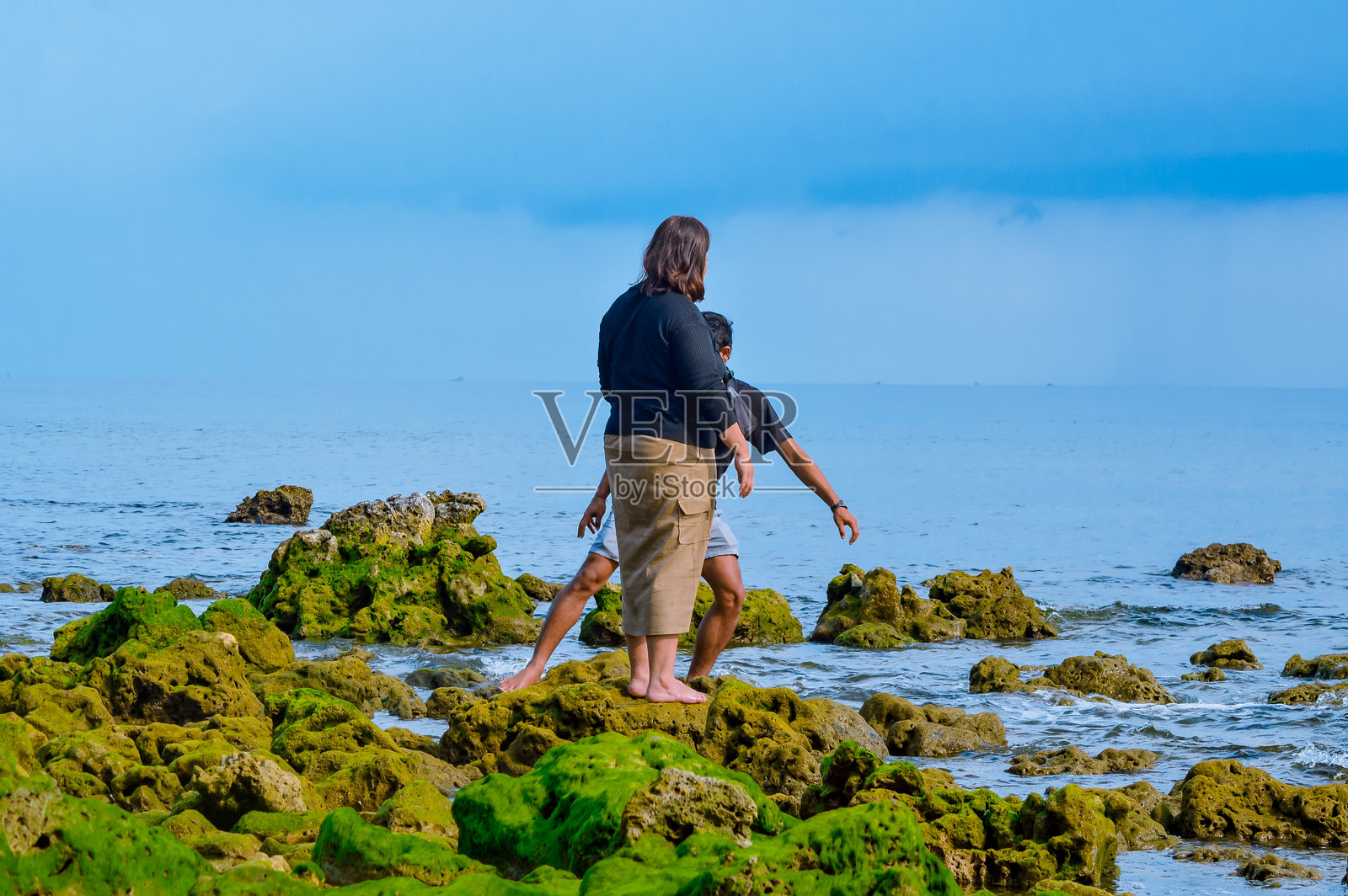 男女在海边的苔藓岩石上保持平衡照片摄影图片