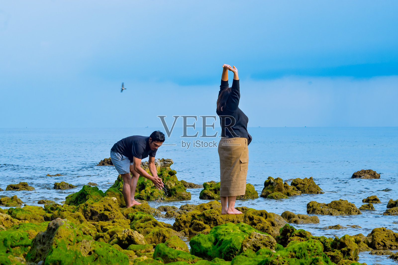 男女在覆盖着绿藻的岩石海滩上享受时光照片摄影图片