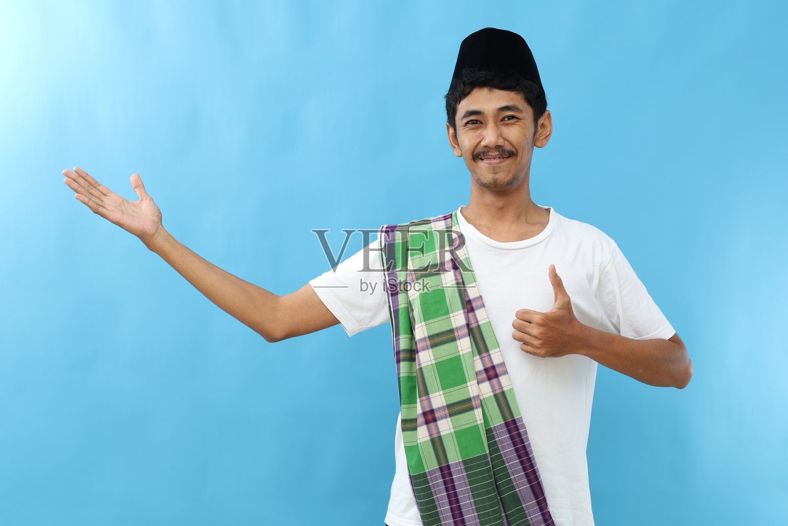 穿着可可服的亚洲穆斯林男子，微笑着举起手掌并竖起大拇指，显得快乐而愉快。照片摄影图片