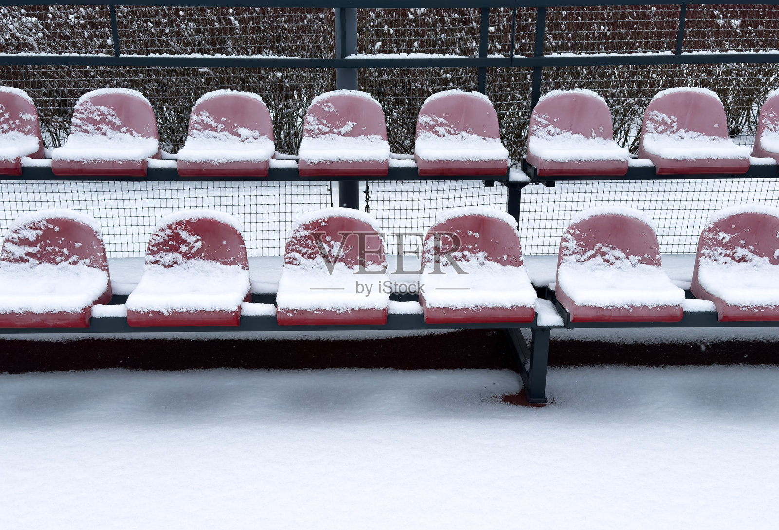 冬季空旷的户外体育场，塑料座椅在钢支架上被雪覆盖照片摄影图片
