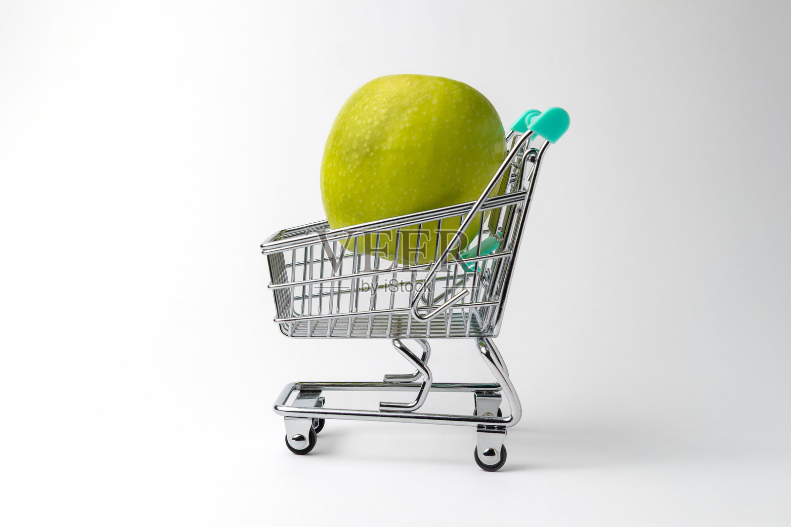 白色背景上的迷你购物车里放着一个绿色苹果照片摄影图片