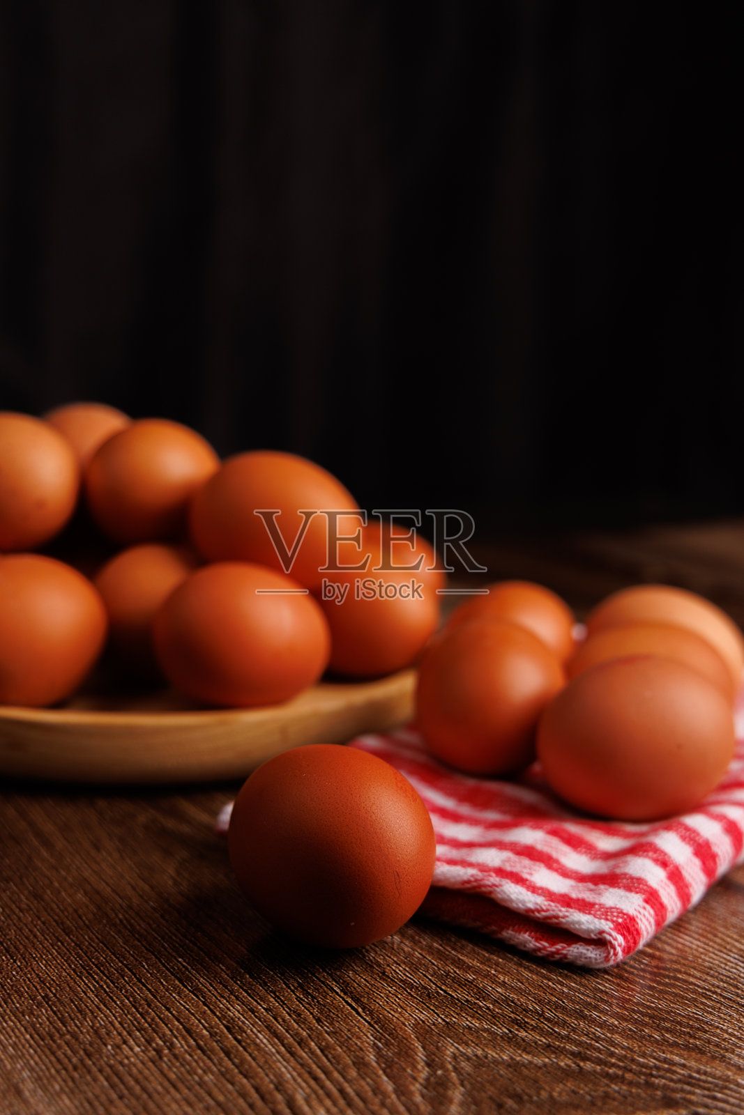 一个装满棕色鸡蛋的天然木盘，放在红白相间的布餐巾上，置于粗犷的木质表面上。照片摄影图片