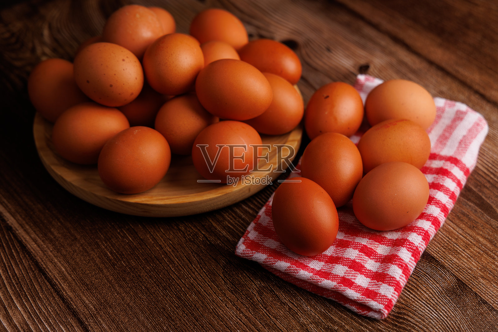 棕色鸡蛋堆放在木盘上，盘子上铺着红白相间的餐巾，放在乡村风格的木桌上，展示了食品价格的上涨。照片摄影图片