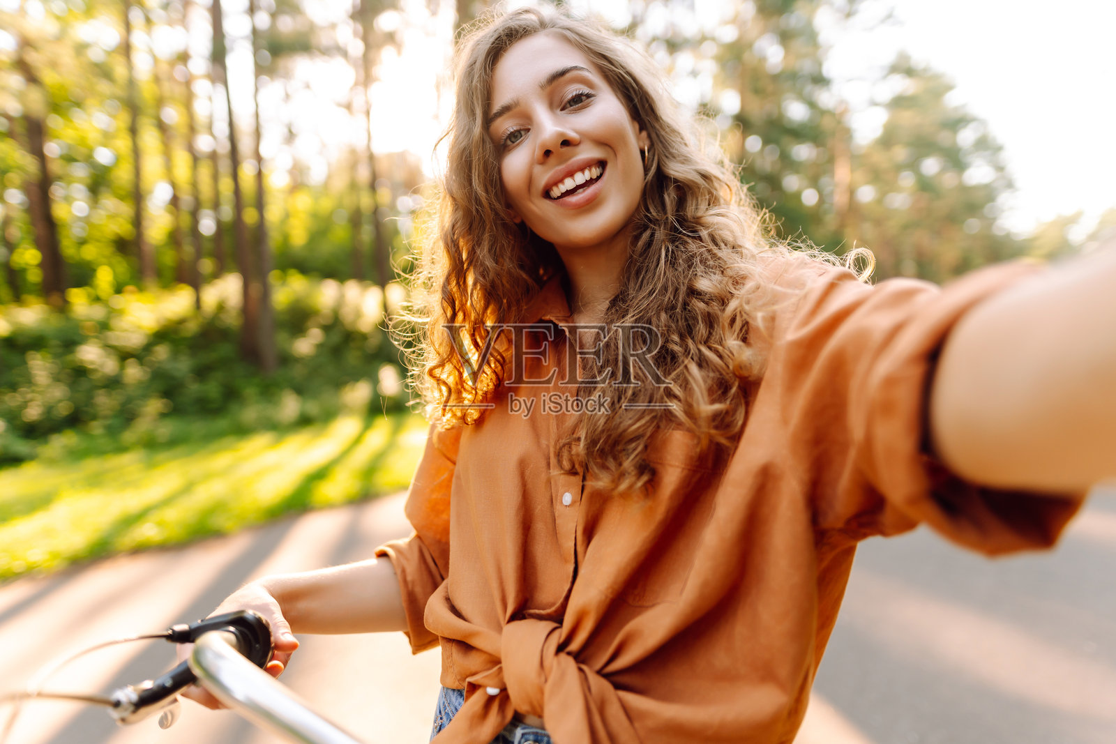 快乐的女性在阳光明媚的公园骑自行车并自拍。照片摄影图片