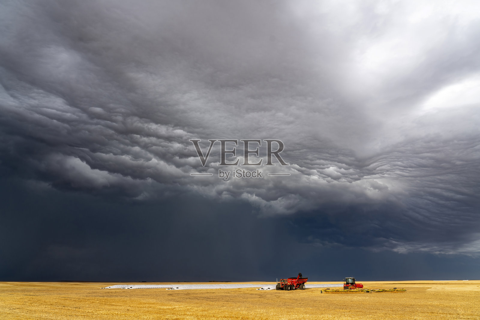 戏剧性的棚云逼近小麦田里的收割机照片摄影图片