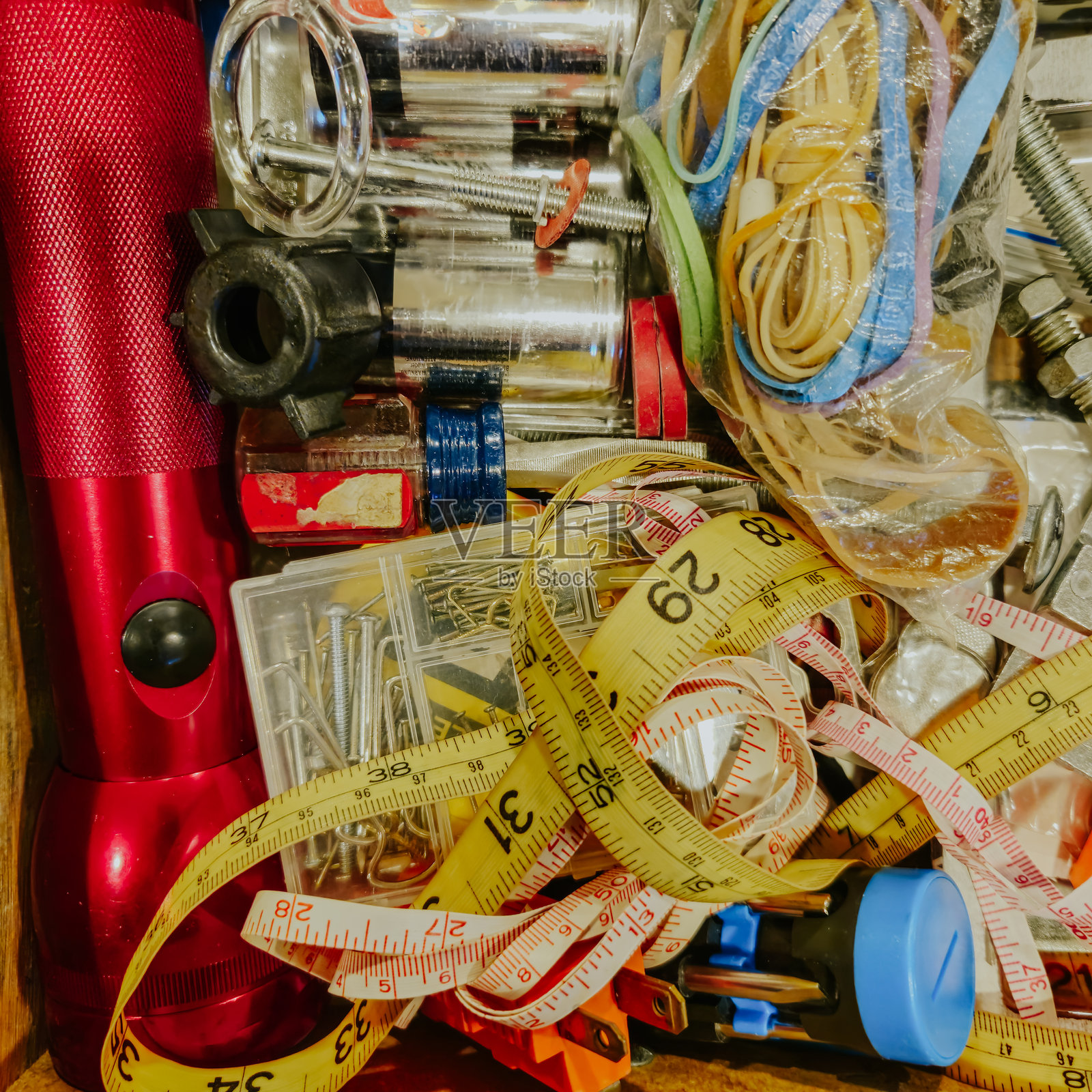 家庭杂物抽屉的特写。随机物品包括卷尺、橡皮筋、螺母、螺栓、钉子、钉子夹、电池和手电筒。照片摄影图片