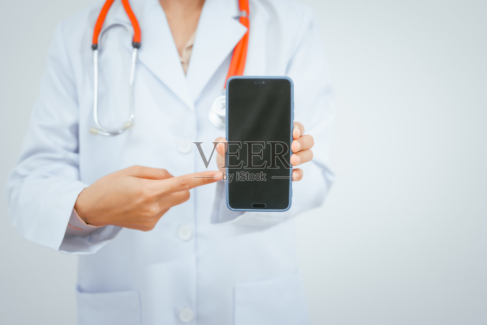 一位年轻的女性医生，穿着白大褂，佩戴听诊器，微笑着站在白色背景前，手持医疗报告，在医生办公室提供在线咨询。照片摄影图片