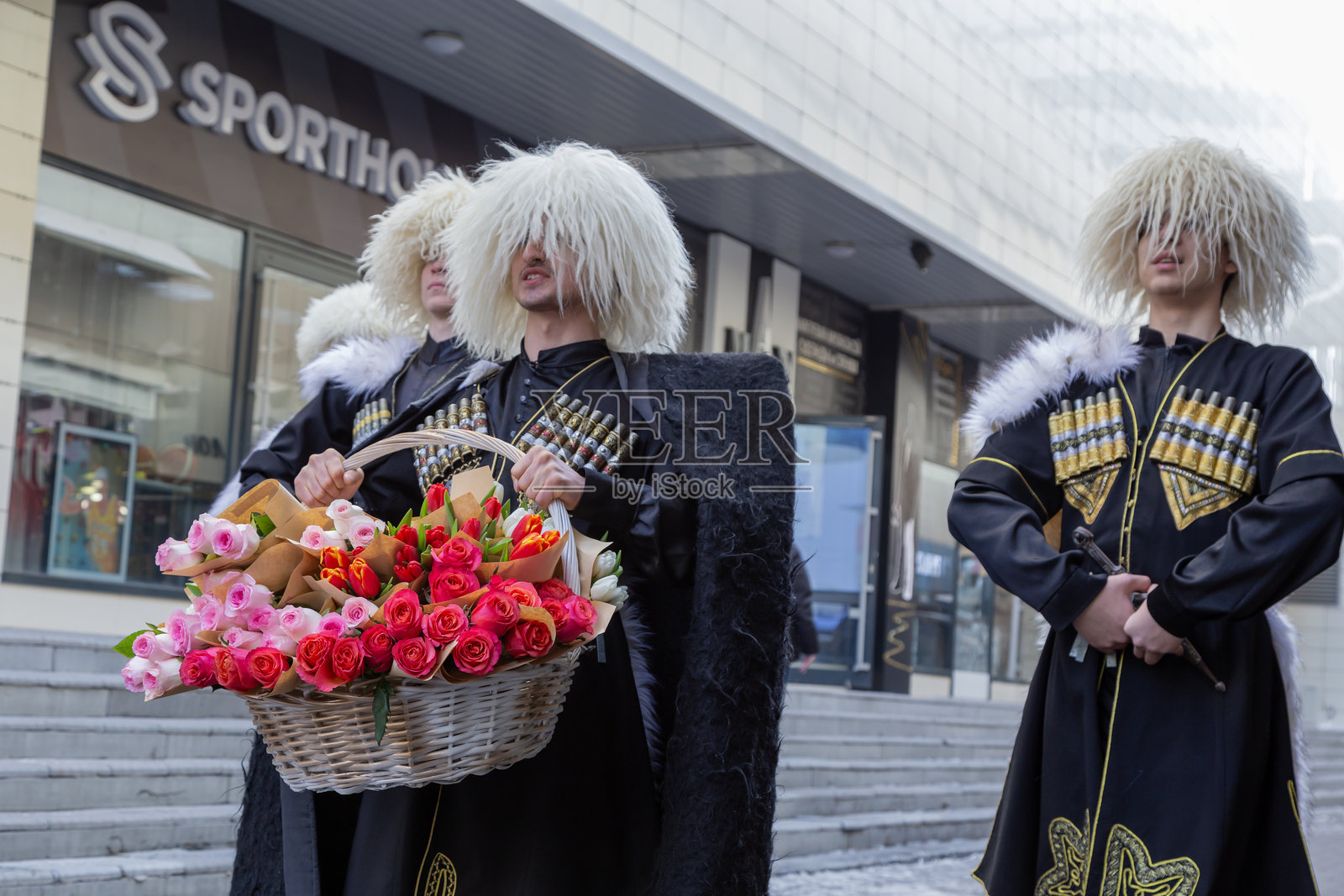 来自车臣的白人男性穿着民族服装在冬季的街道上跳舞，手里拿着花篮祝贺女性国际妇女节。照片摄影图片