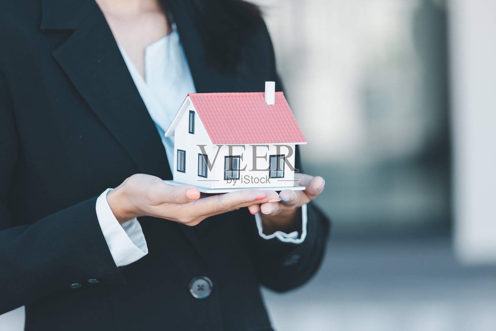 女性手握钥匙，购买房屋模型，商业概念涉及销售、财务管理、投资银行贷款、所有权、收入、经济、金融投资和公寓购买，模糊背景为房地产。照片摄影图片