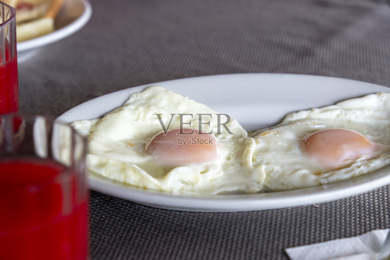 一盘白色盘子里的两个煎蛋，旁边是盛着红色果汁的杯子照片摄影图片