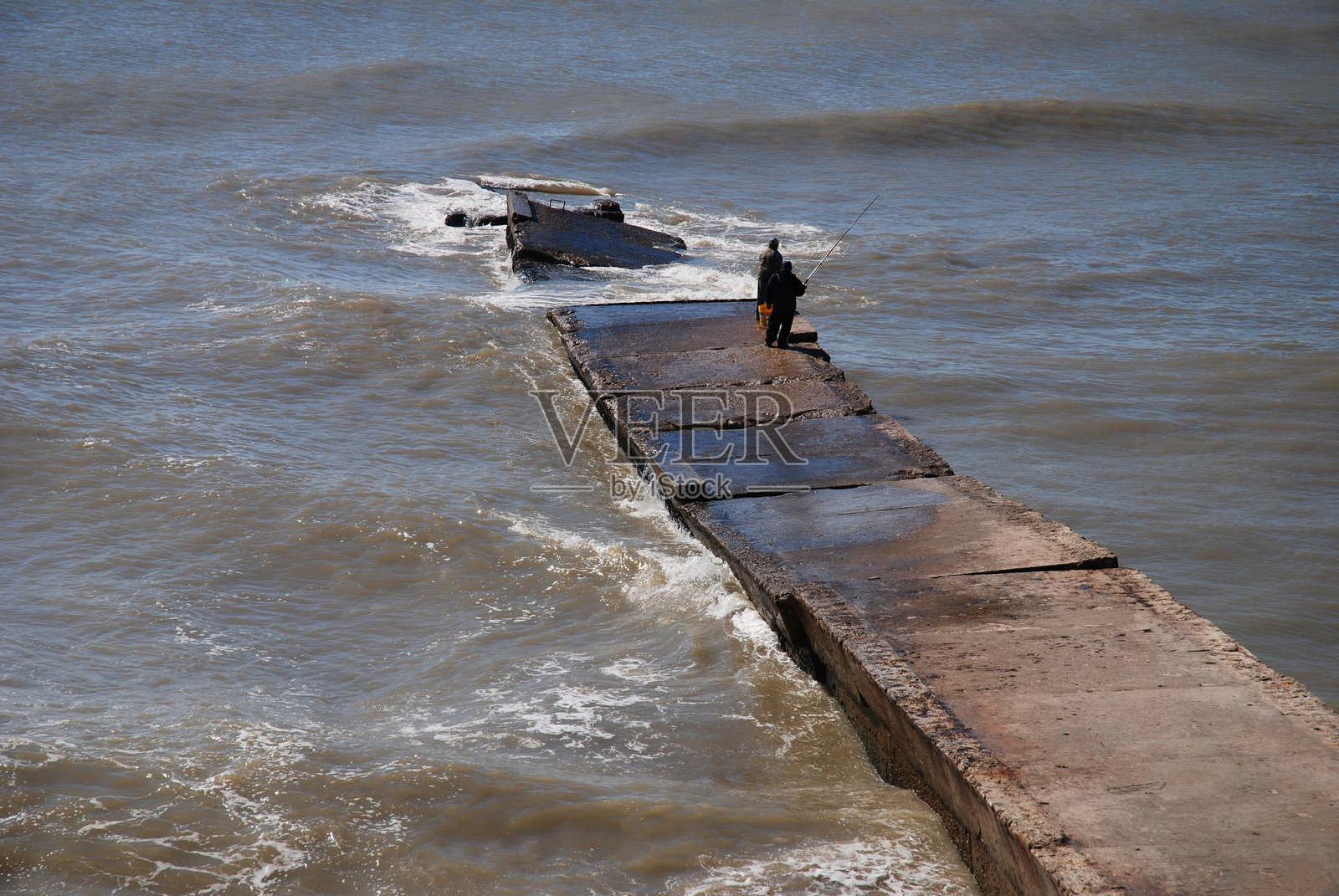 石头码头延伸至大西洋的水域。在结构的尽头，两位渔民站着。照片摄影图片