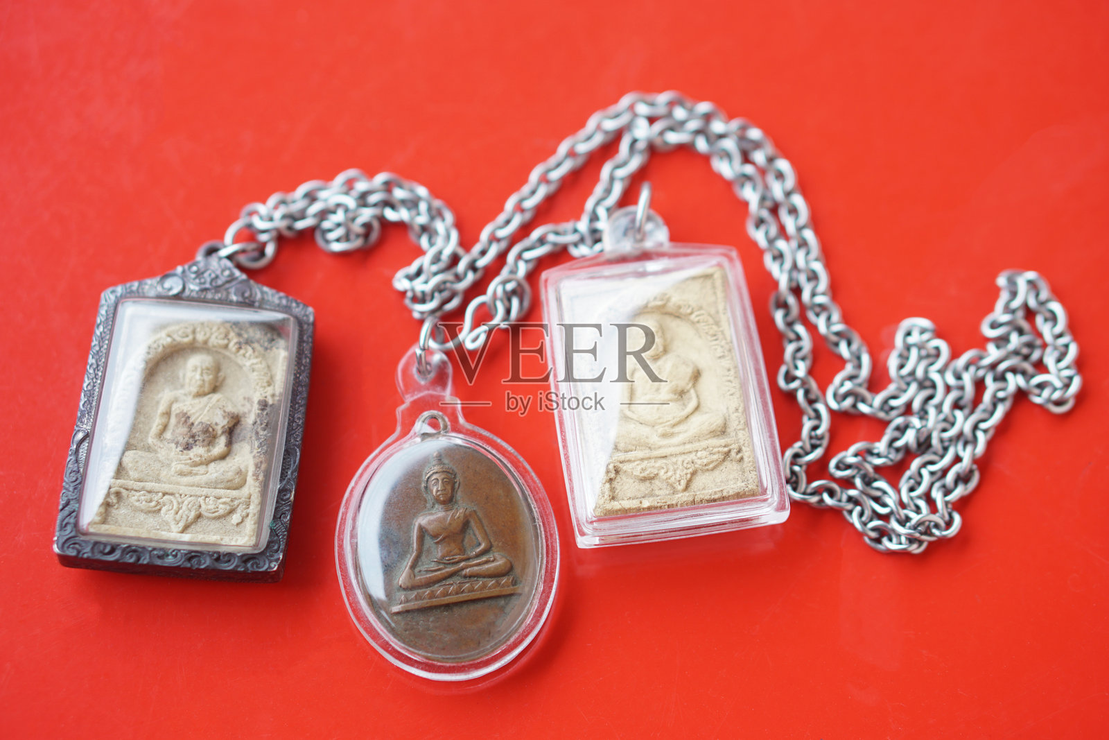 红色背景上的泰国佛教护身符。佛教的概念、信仰和信念，旨在保护人们免受危险，带来好运、商业繁荣和财富。收集护身符作为一种爱好或进行交换。照片摄影图片