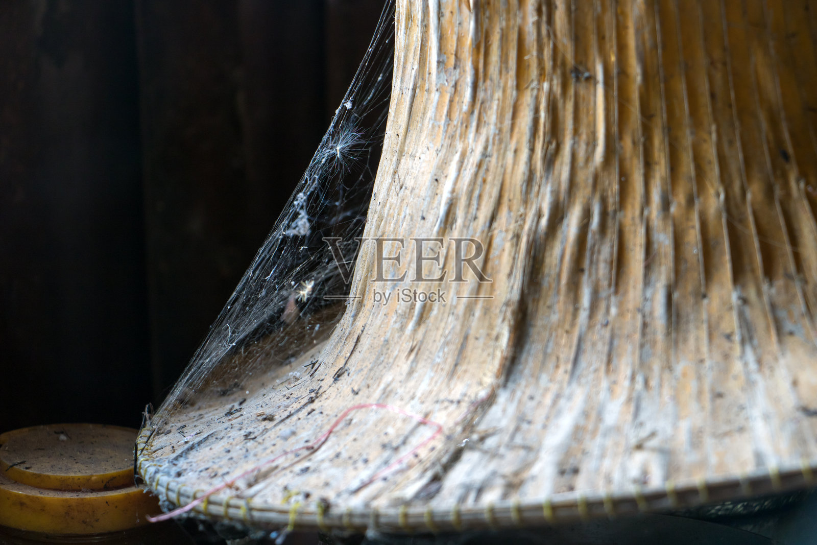 草帽上的蜘蛛网特写。泰国乡村房屋衣橱里的旧物品。照片摄影图片