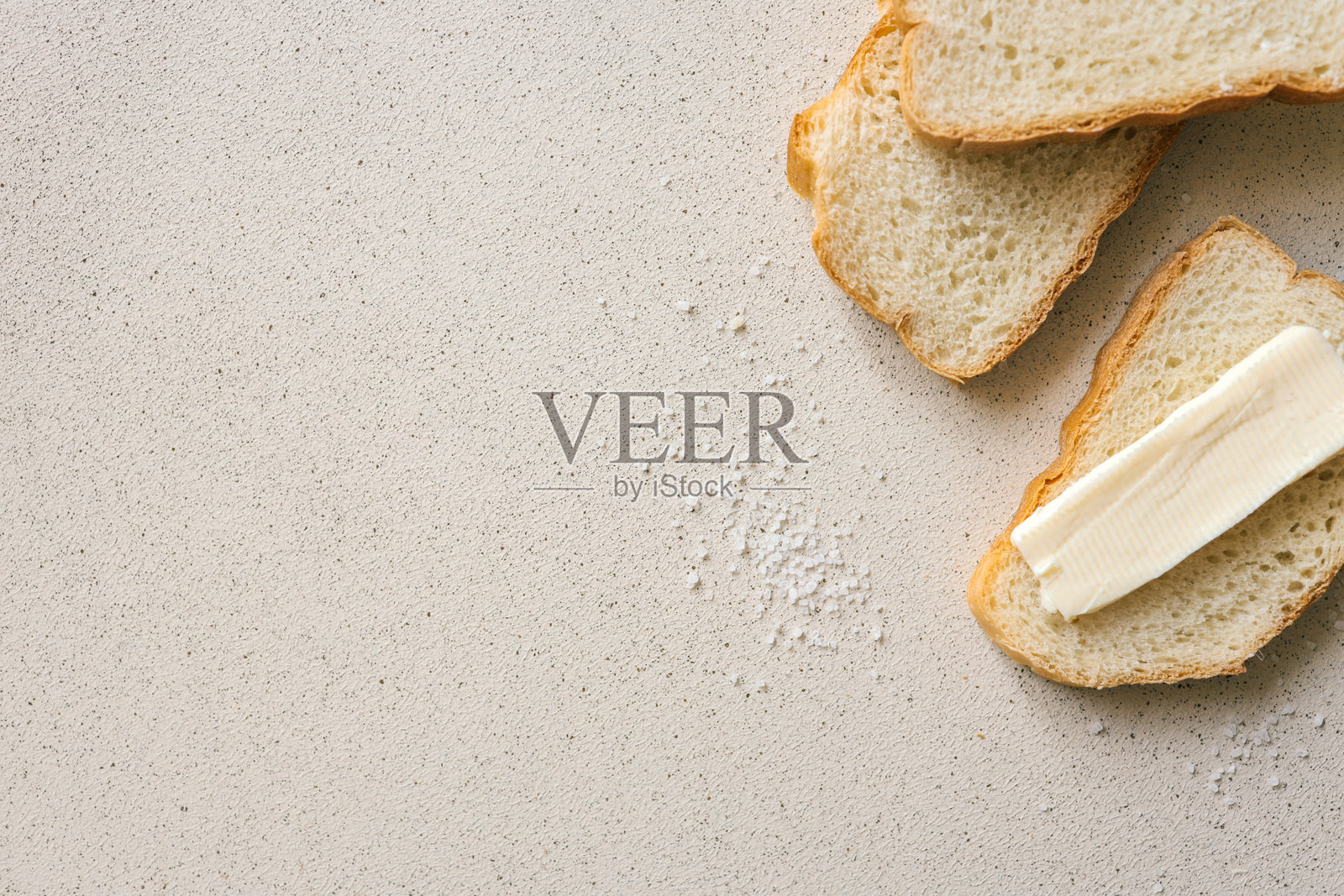 一片新鲜的面包上涂抹着厚厚的黄油，旁边有一把黄油刀，撒着盐的纹理表面。简单而质朴的食物准备，突显自制早餐或小吃的必备元素。照片摄影图片