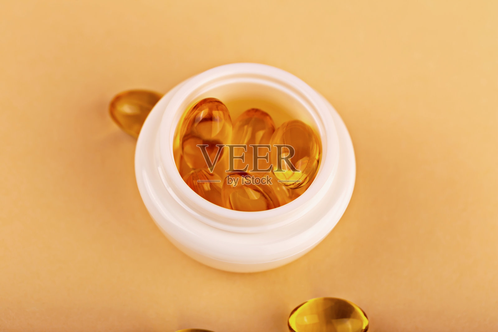 打开的化妆品瓶，里面装满了金色软胶囊，背景为米色。护肤、健康和美容补充品照片摄影图片