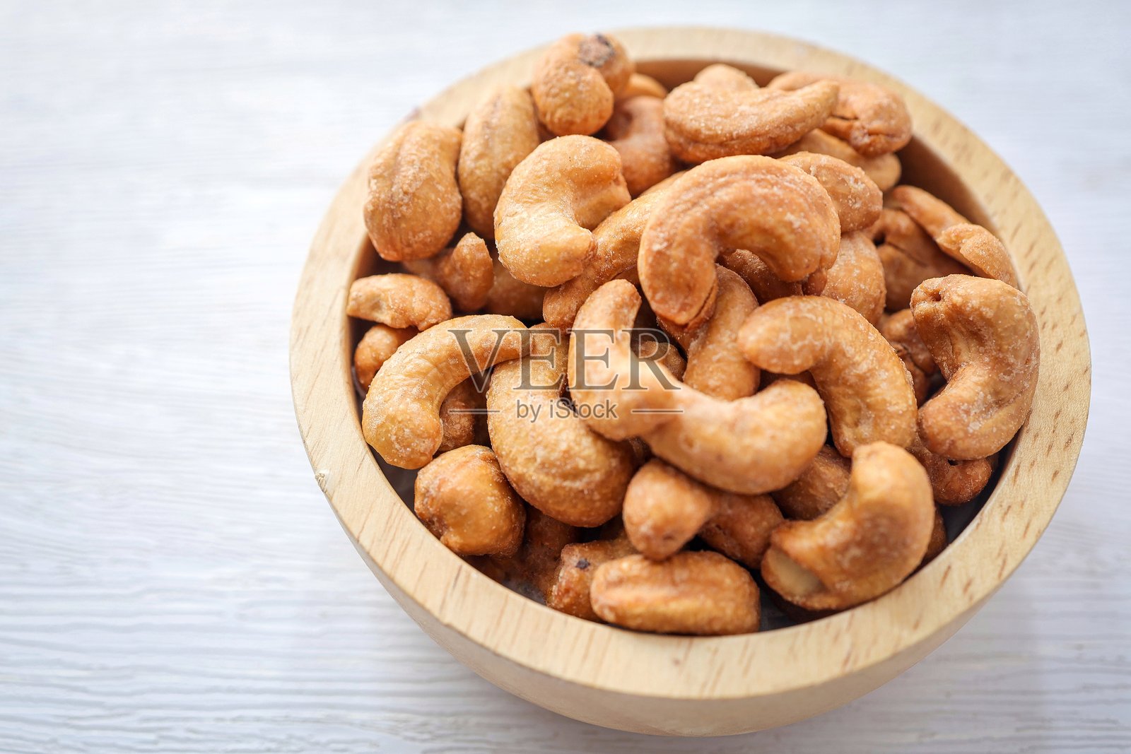 白色背景上的木碗里装着咸腰果照片摄影图片