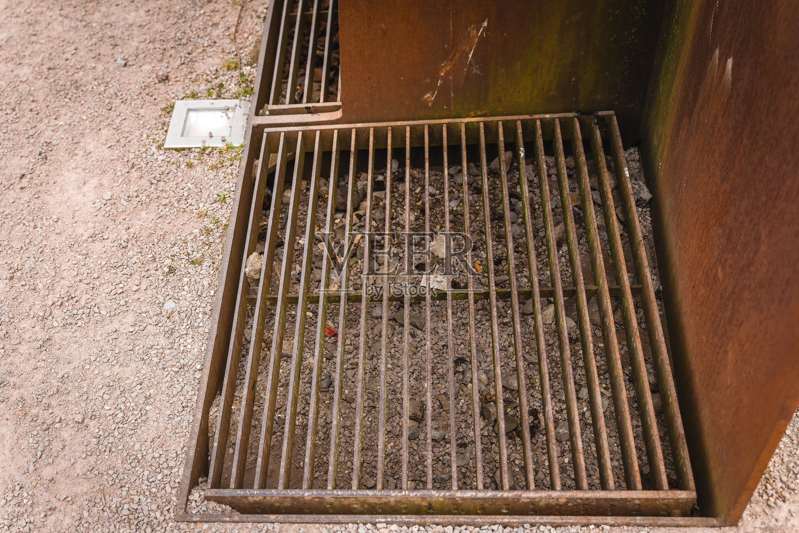 户外区域的碎石小径旁边有一个生锈的金属格栅，下面积聚了杂物。照片摄影图片