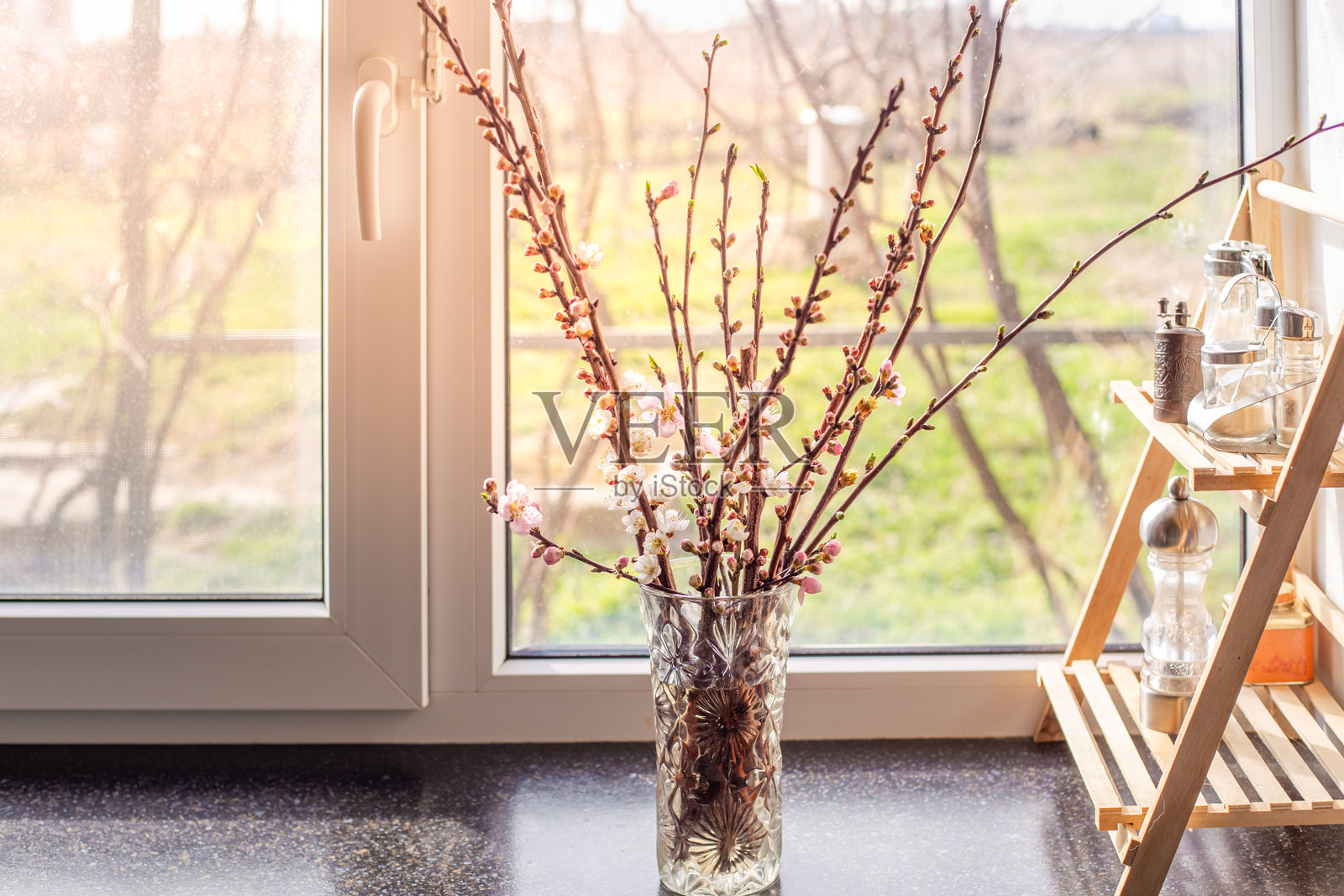 春天的一天，厨房台面上窗边的花瓶里插着开花的果树枝。照片摄影图片