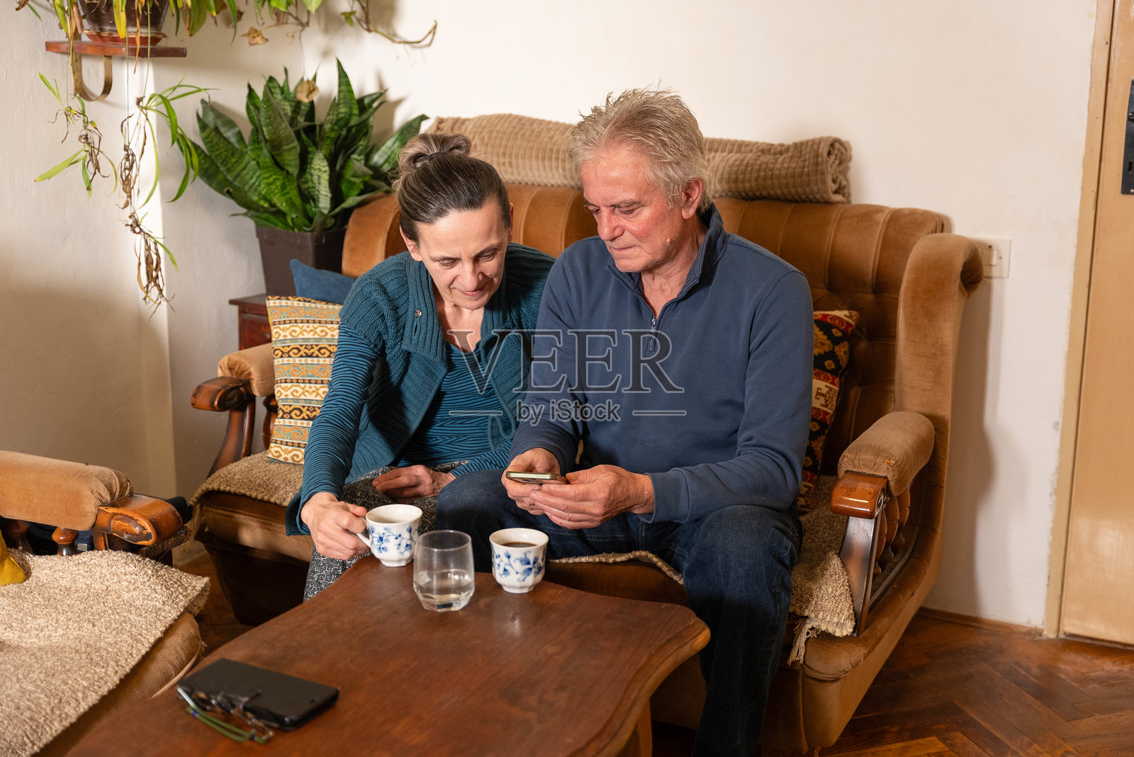 老年夫妇在家中使用智能手机并喝茶照片摄影图片