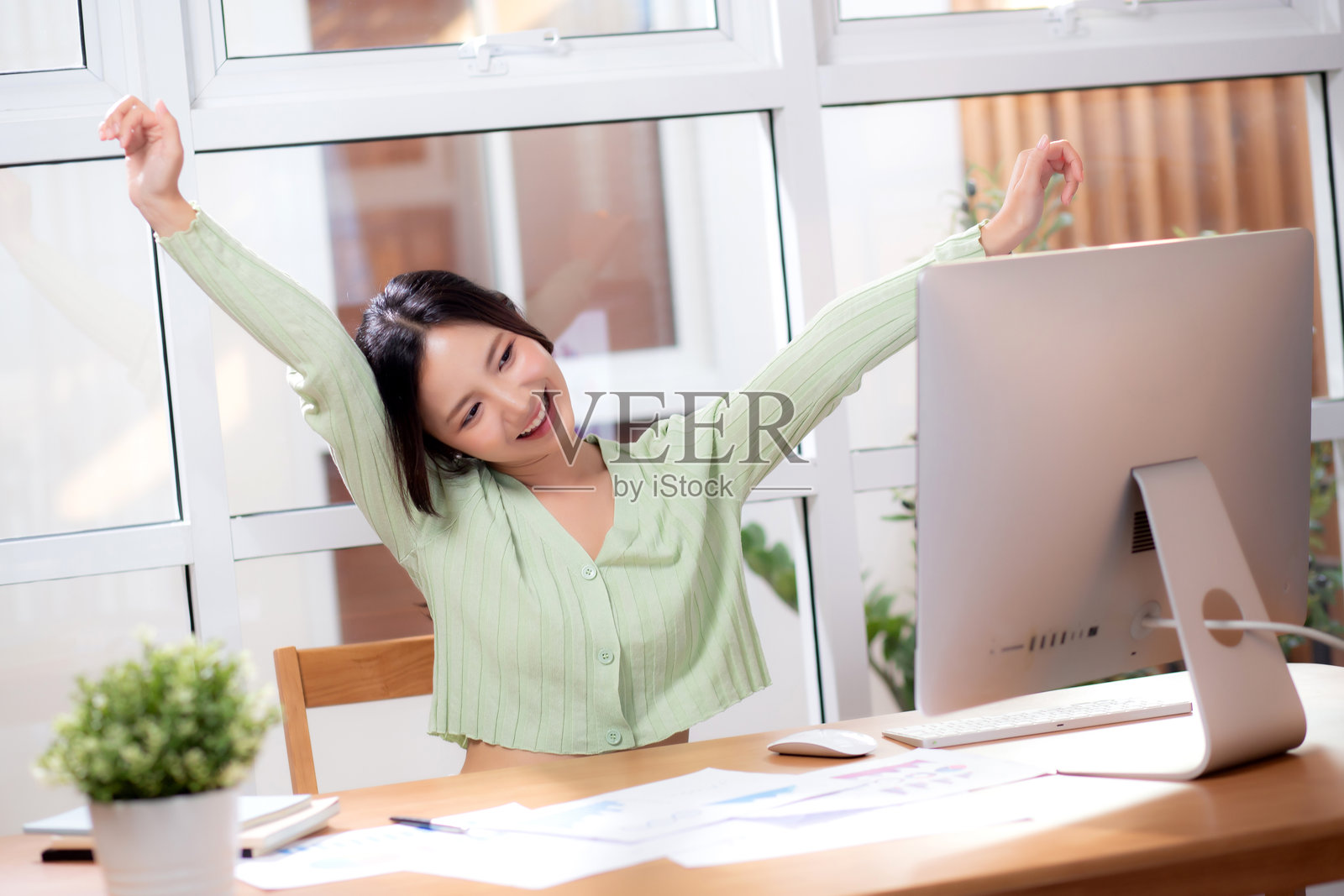 年轻的亚洲女商人在现代家居办公室使用台式电脑取得成功，女商人在家中的客厅里使用台式电脑工作，感到胜利和满意，商业概念。照片摄影图片