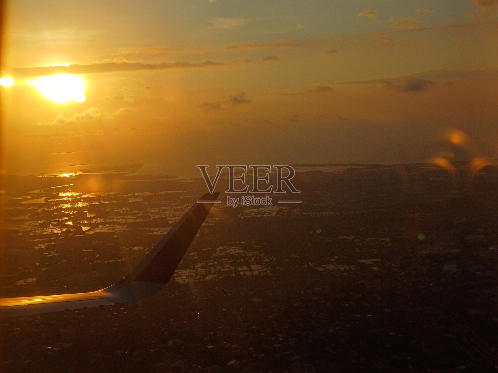 从飞机窗户俯瞰金色日落下的海滨城市景观照片摄影图片