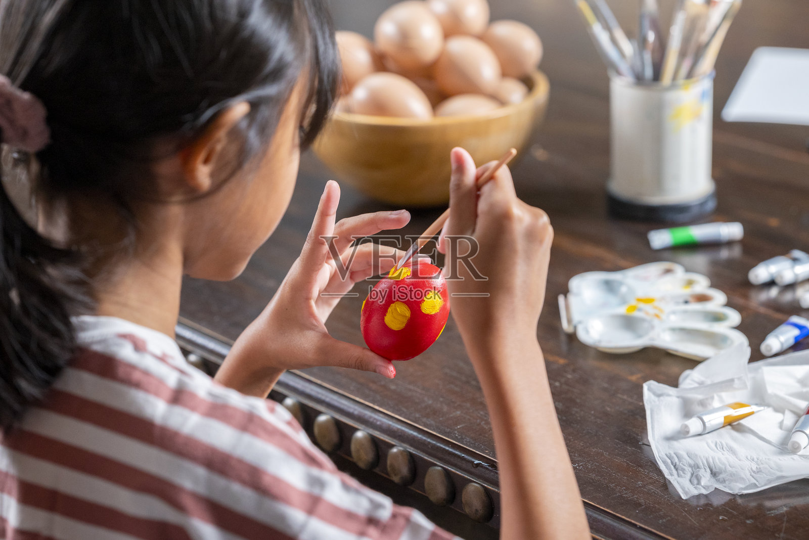 东南亚的小女孩正在桌子上用画笔为复活节彩蛋装饰。庆祝复活节假期的概念。照片摄影图片