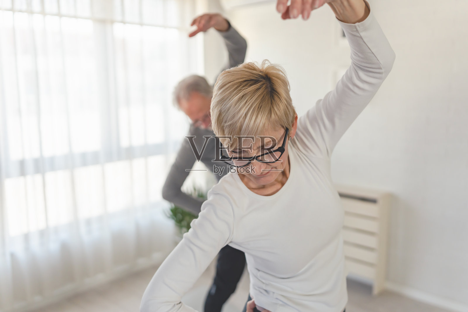 老年夫妇在家锻炼，在明亮的客厅里做侧身拉伸。他们面带微笑，参与健康活动以保持活力和灵活性。照片摄影图片