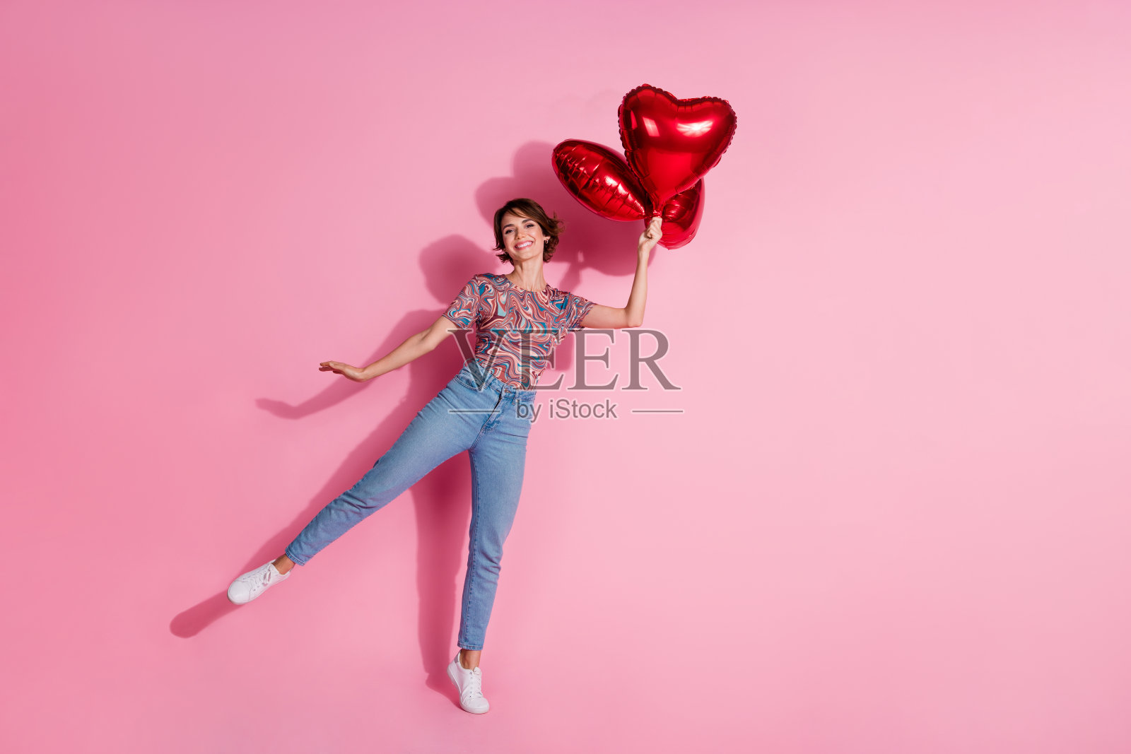 可爱迷人的女孩穿着时尚的衣服，手持氦气球，背景为粉色。照片摄影图片