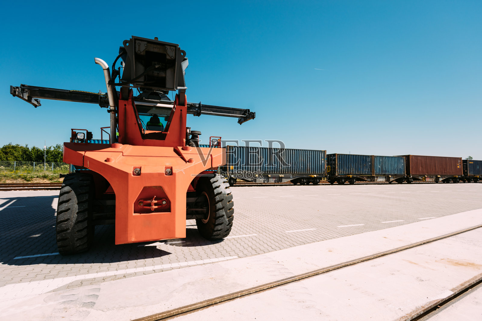 蓝天下，工业集装箱升降机在货车旁的路面上。照片摄影图片