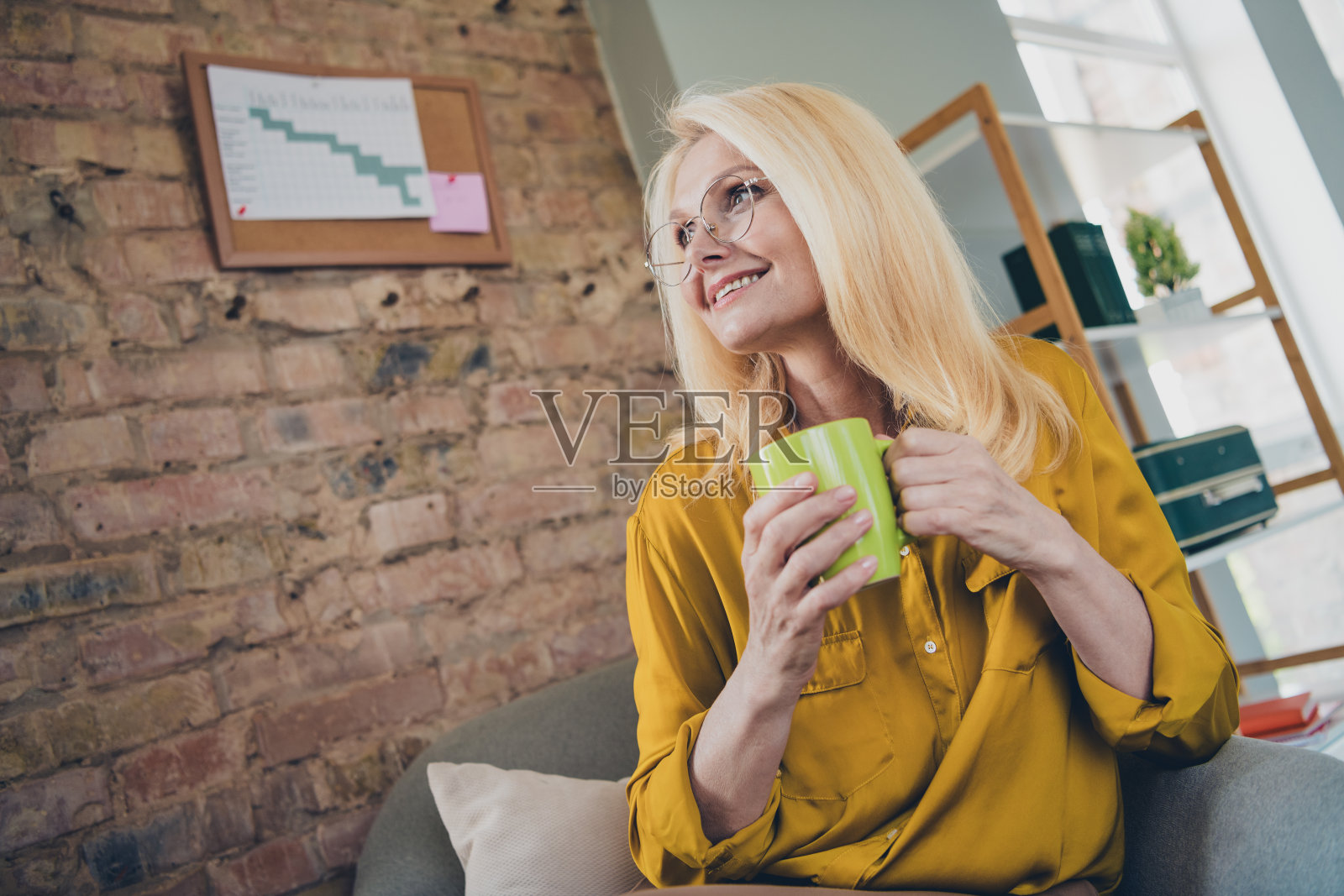 积极心态的女性专家穿着衬衫，微笑着在室内工作站喝咖啡照片摄影图片