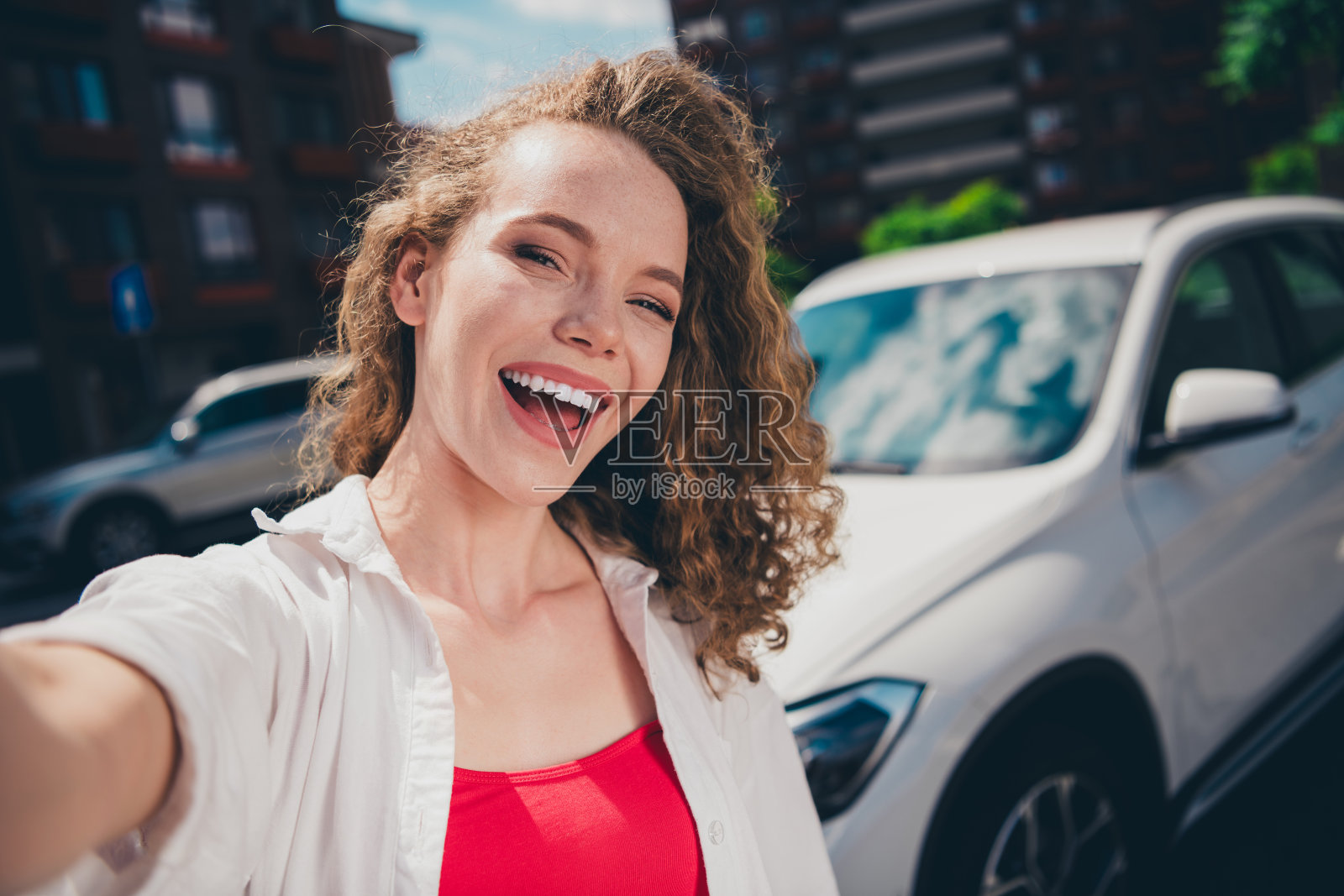 兴奋而梦幻的女士自拍照，面带愉快的微笑，穿着白衬衫，在现代城市街道上行走。照片摄影图片