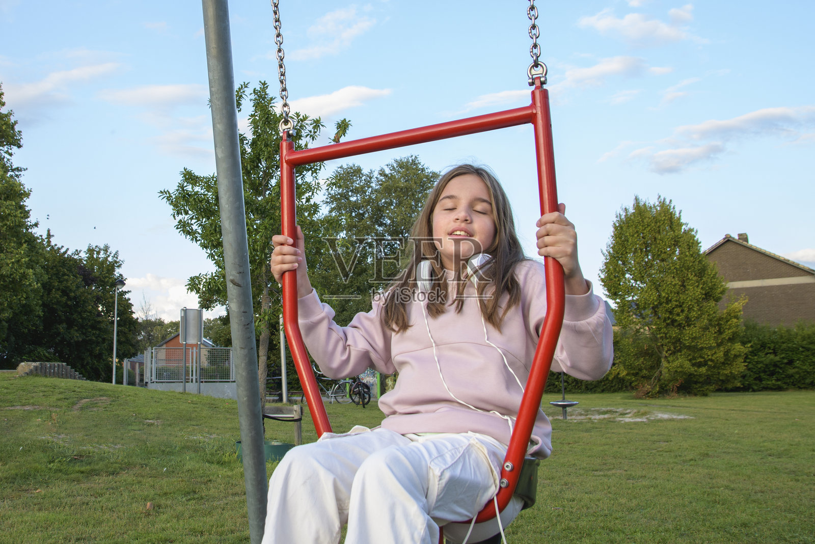 一个夏天的公园里，少女在秋千上尽情享受骑行的乐趣。照片摄影图片