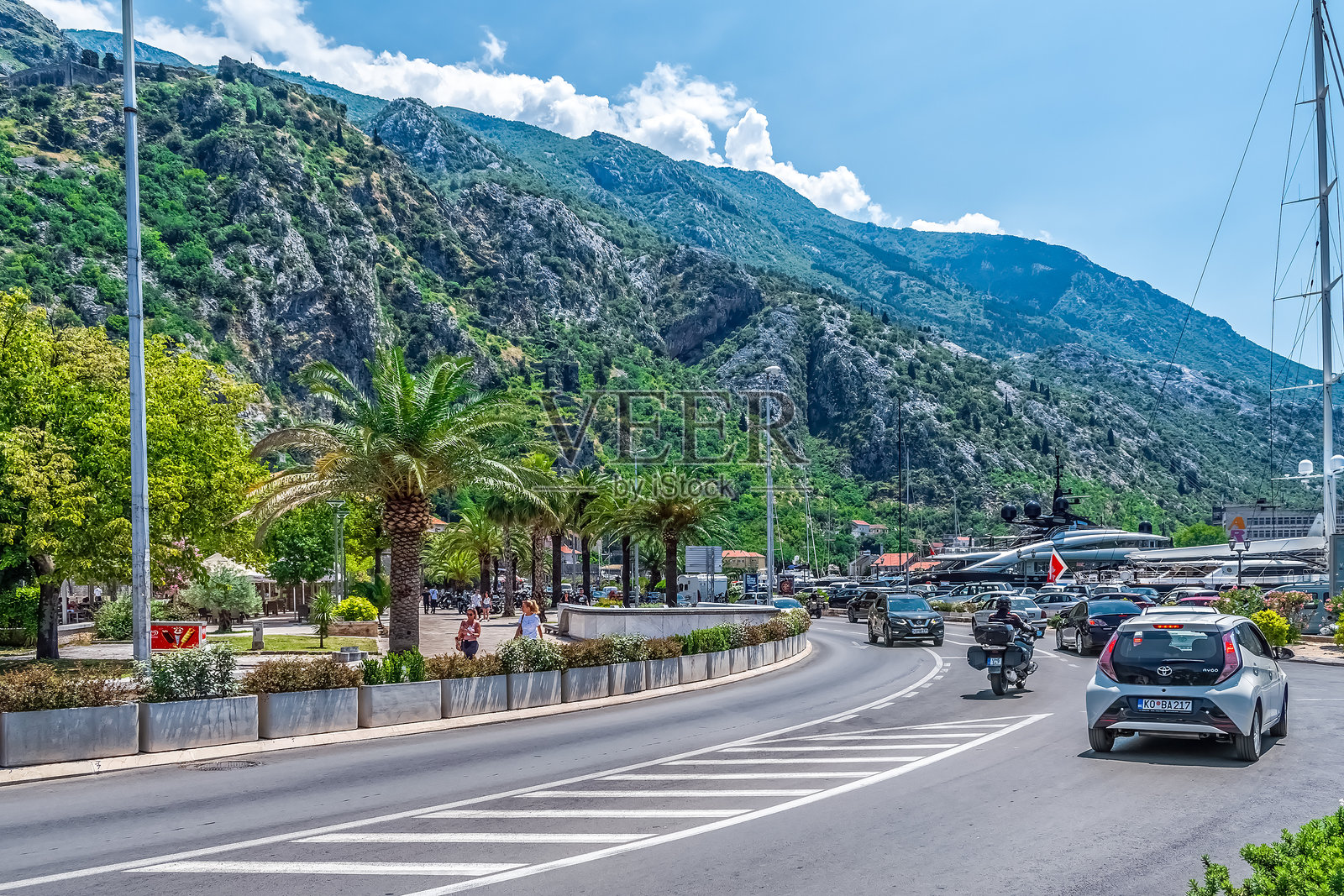 科托尔的阳光明媚的一天，风景如画的街道两旁种满了棕榈树，远处是群山，还有繁忙的游艇码头。照片摄影图片