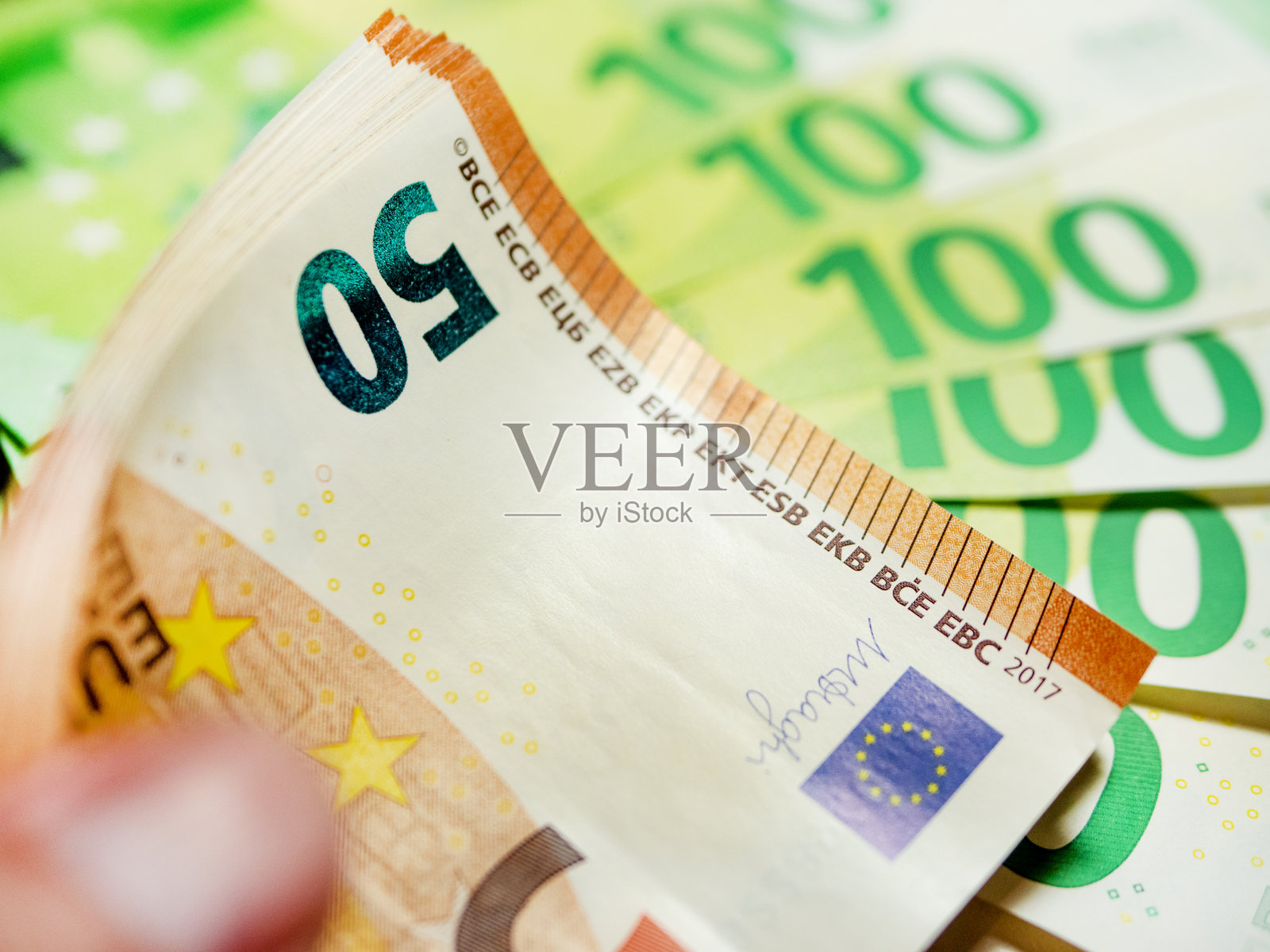 男性手中握着一捆欧元，背景模糊照片摄影图片