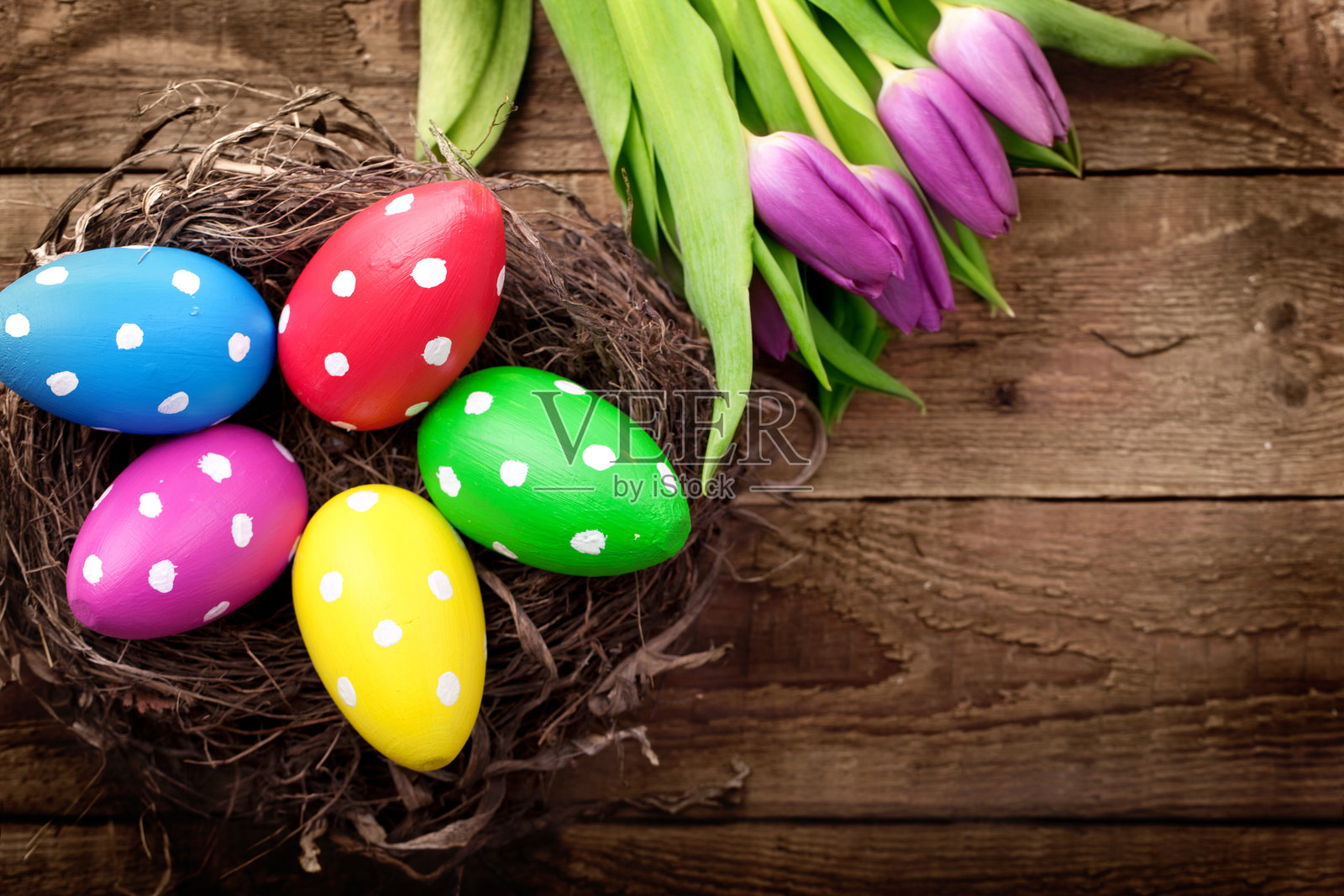 手工绘制的木制复活节彩蛋放在自然巢中，旁边有郁金香，置于木板上照片摄影图片
