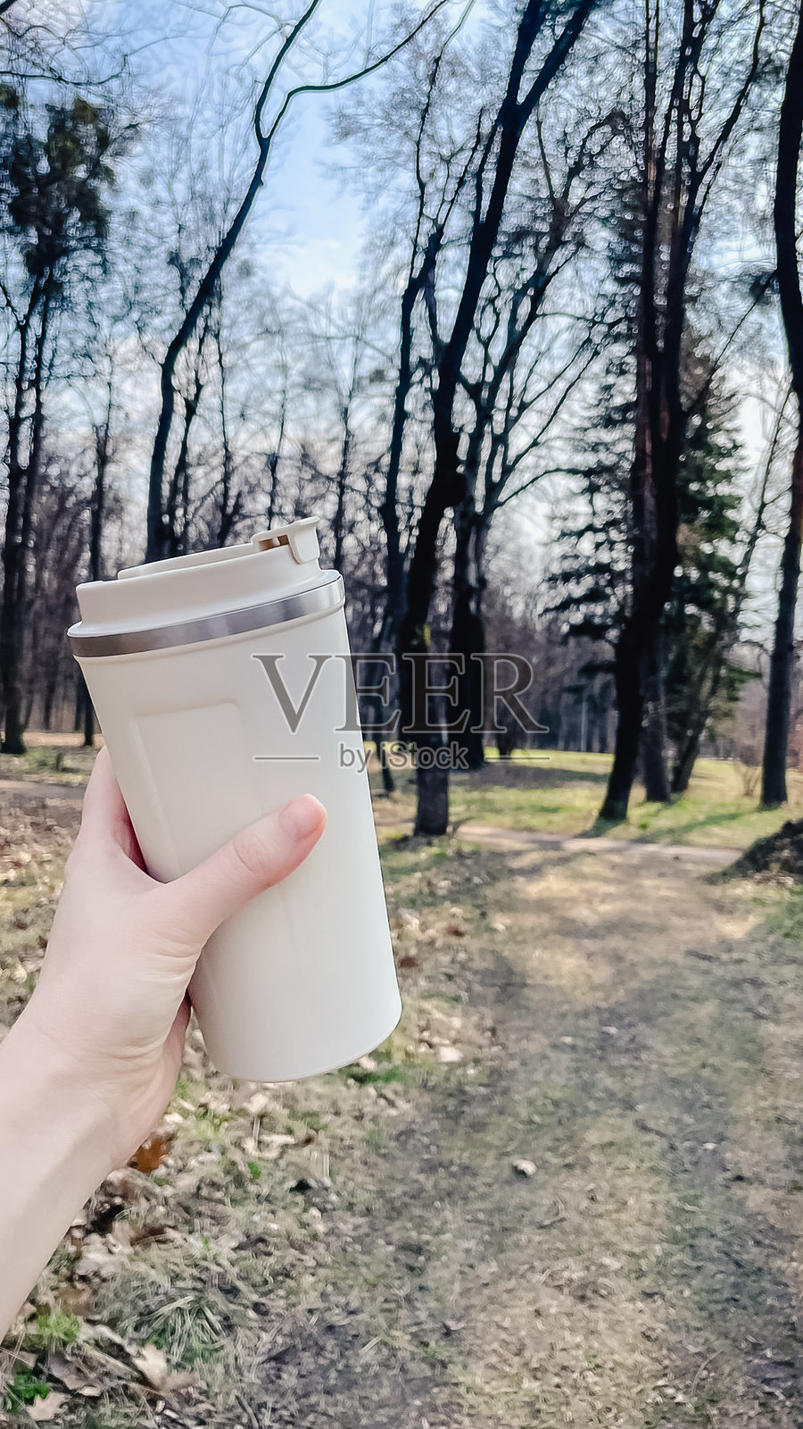 手中拿着米色保温杯在公园散步照片摄影图片