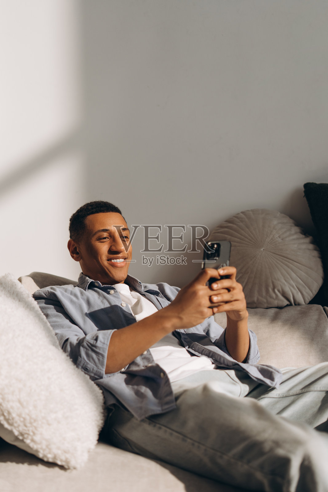 年轻的拉丁裔男子在家中沙发上放松，使用手机。照片摄影图片