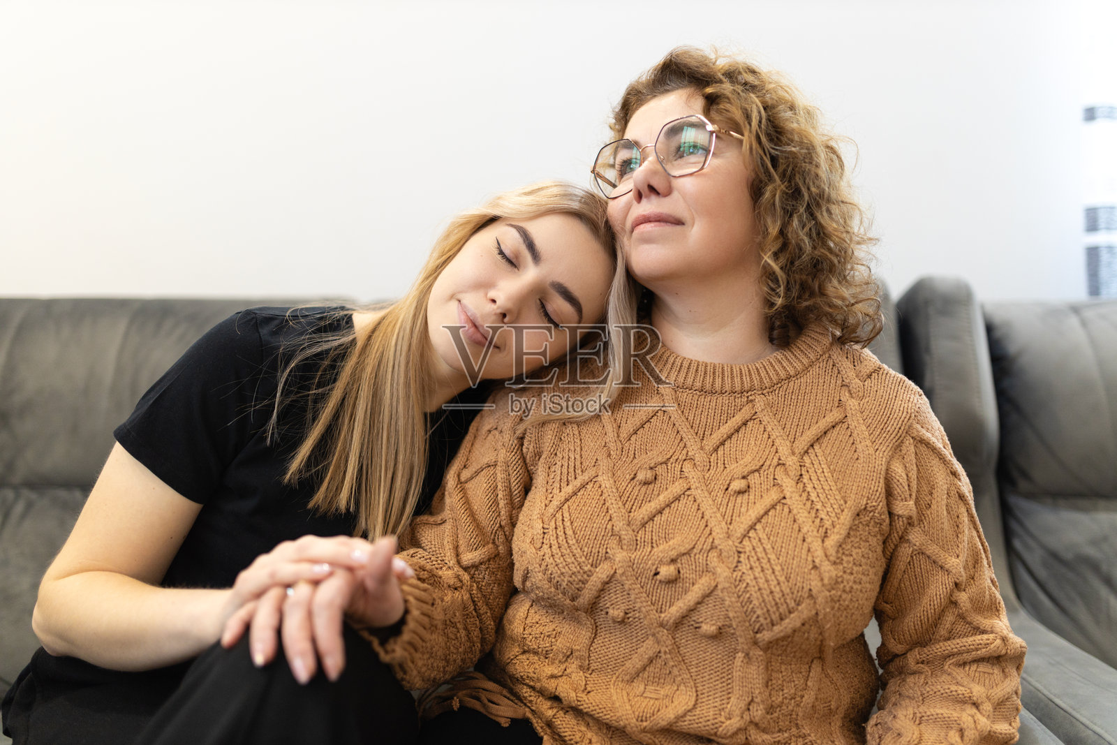 一个开心微笑的女儿坐在客厅的沙发上，正和她的妈妈拥抱。照片摄影图片