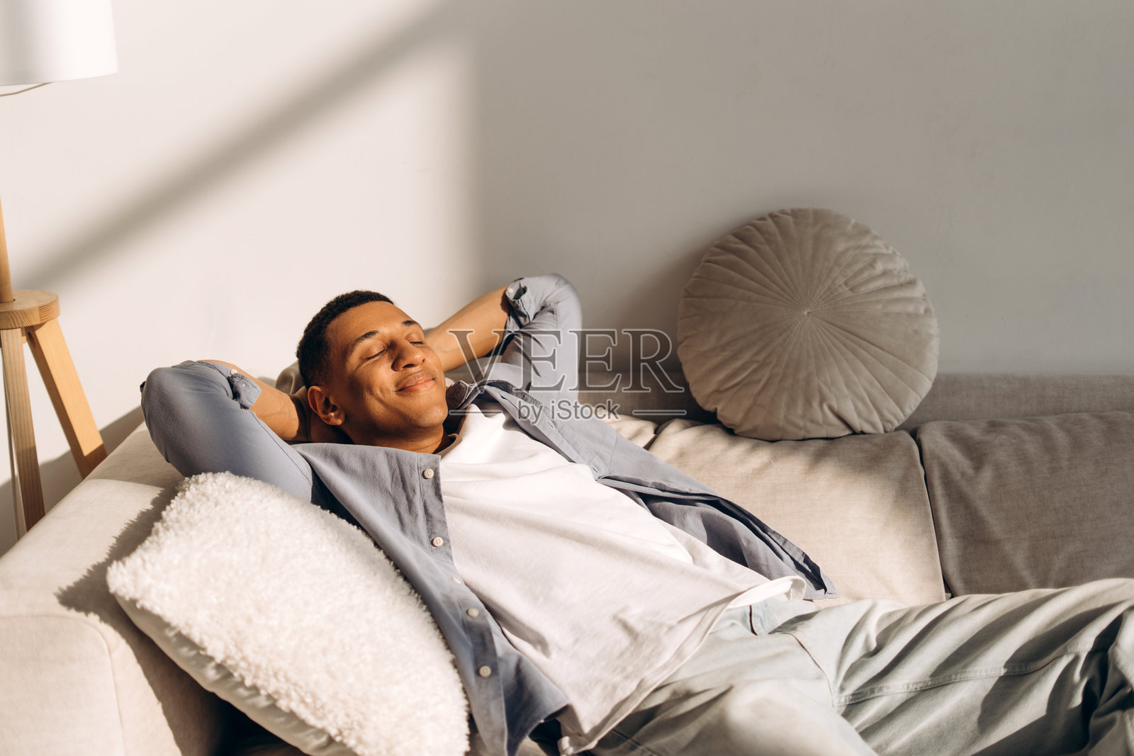 年轻男子在客厅的沙发上放松，享受阳光。照片摄影图片