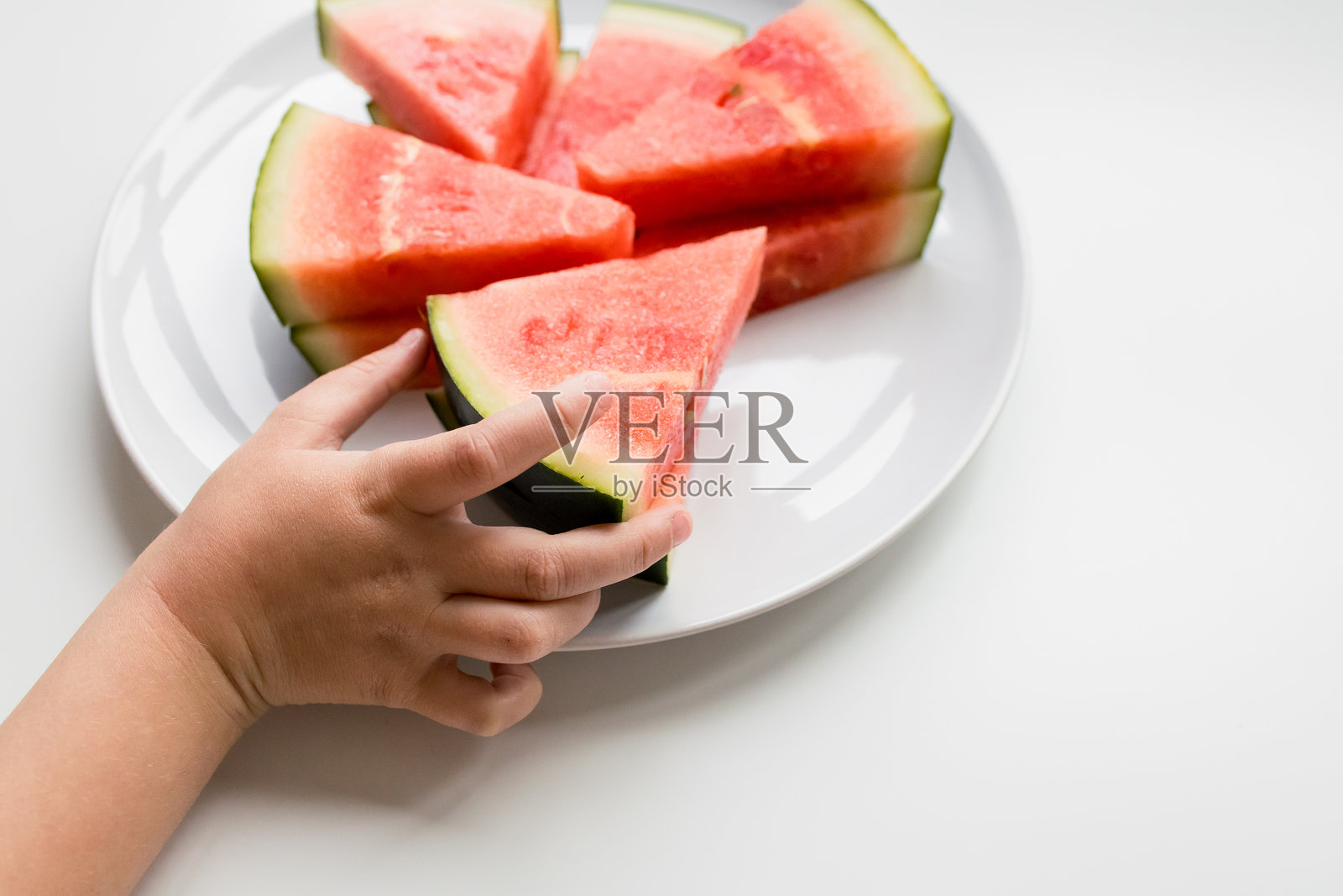 孩子的手伸向白盘上的新鲜西瓜片照片摄影图片
