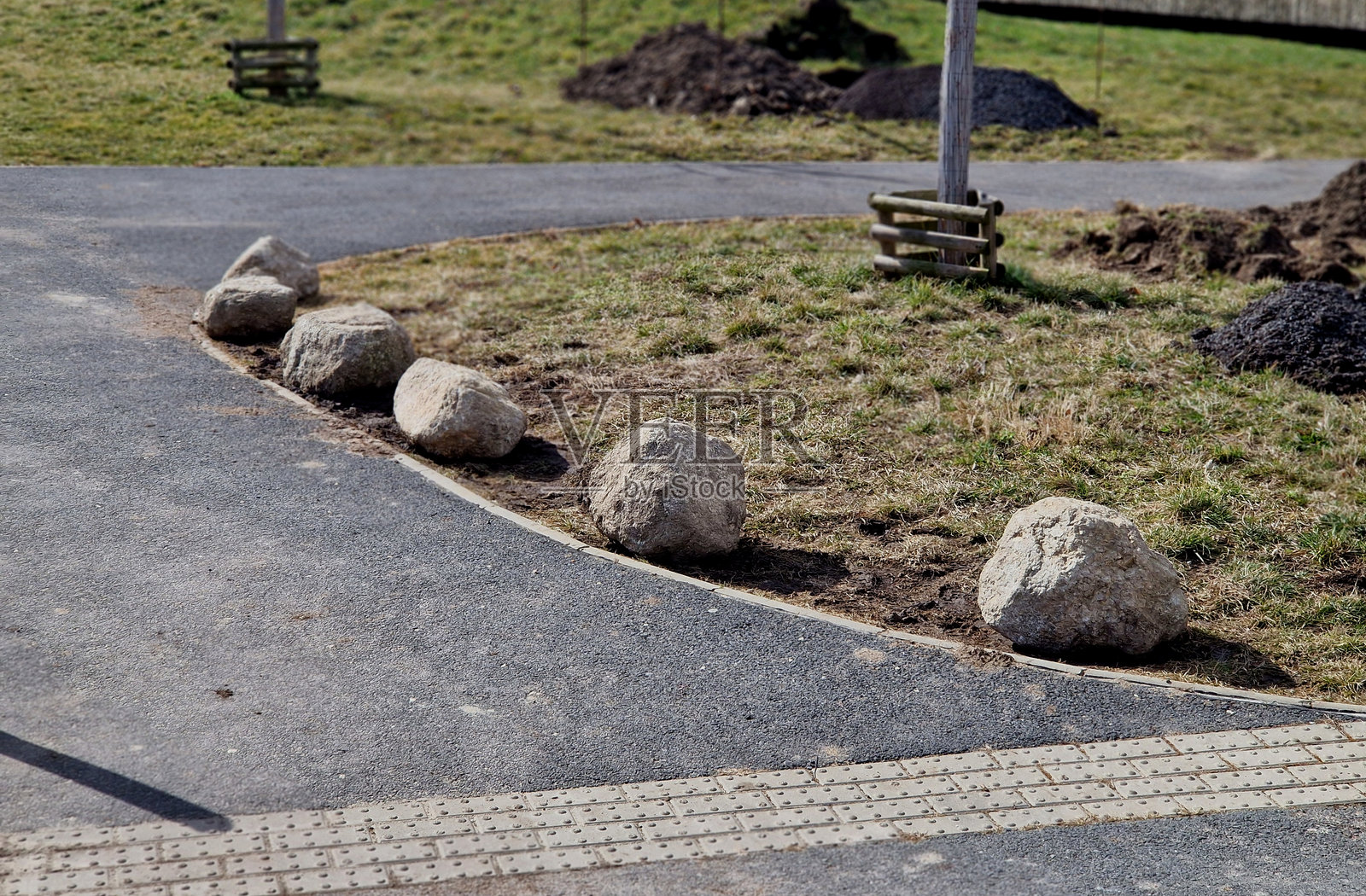 车道之间的灰色石头作为停车保护。乡间道路和自行车道的停车场交通解决方案。沥青表面和草坪，锁定金属柱。红色条纹。照片摄影图片