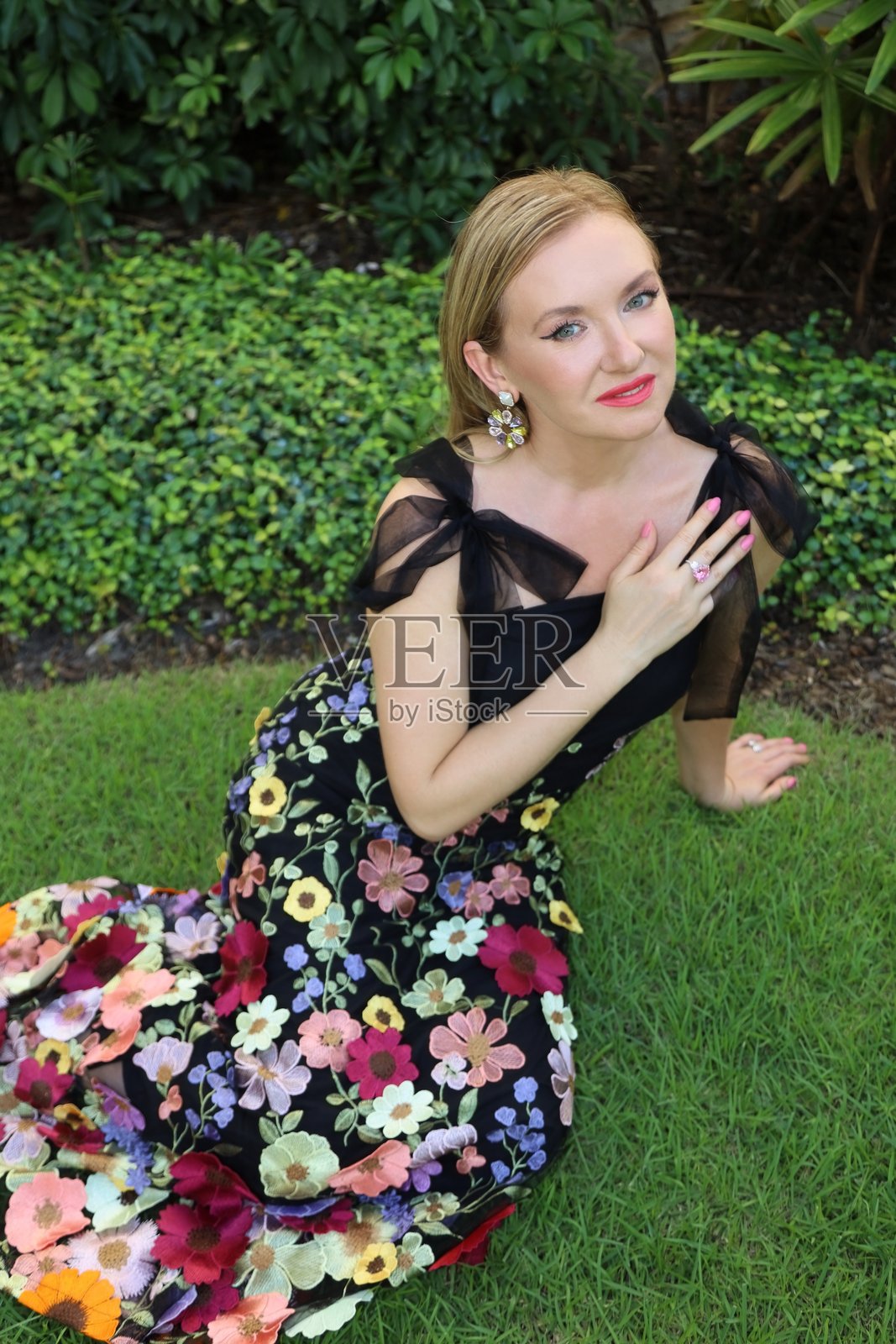 华丽的年轻女性躺在草地上，穿着一袭绝美的黑色特别晚礼服，装饰着花朵。照片摄影图片