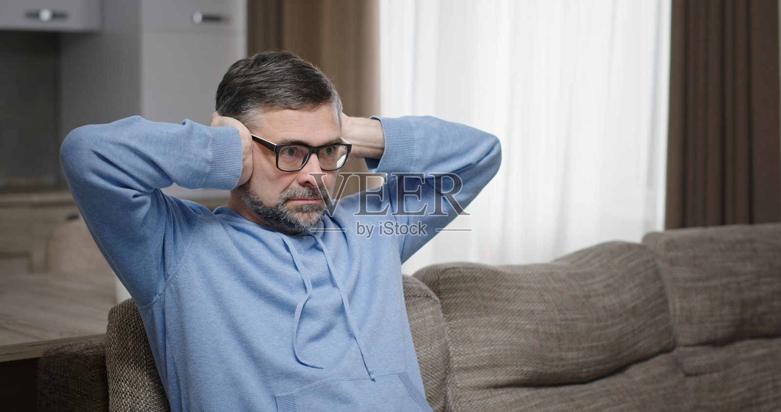 一个坐在沙发上的男人捂住耳朵，感到压力，周围充满了与冲突相关的情绪。照片摄影图片