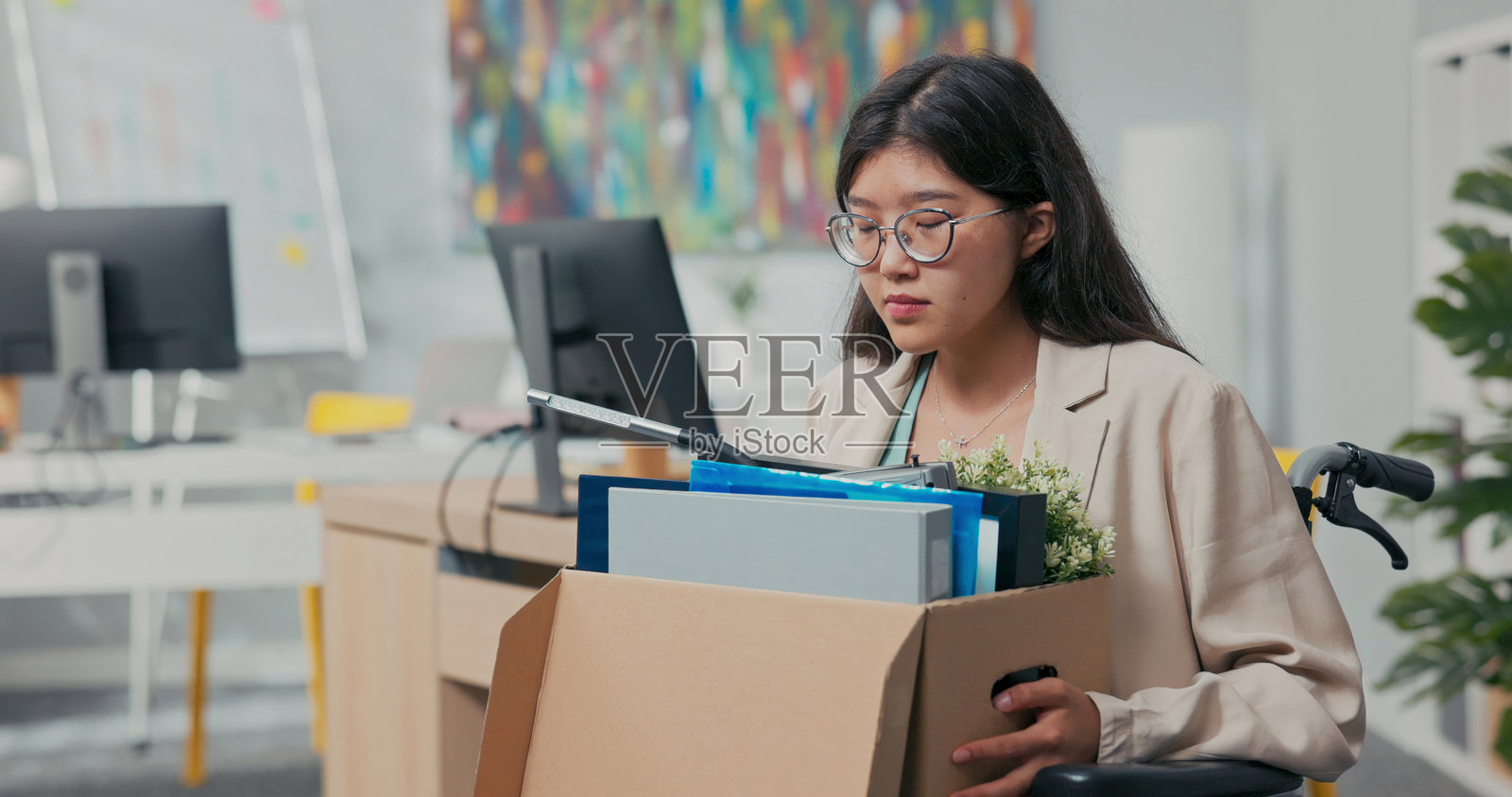 一位戴眼镜的年轻女性坐在轮椅上，因残疾和疾病被解雇，感到雇主的不公和失业的沉重。照片摄影图片