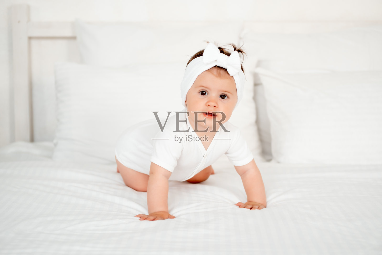 微笑的小女孩或婴儿穿着白色连体衣在床上欢快地玩耍，健康快乐的宝宝在卧室，留有文字空间照片摄影图片