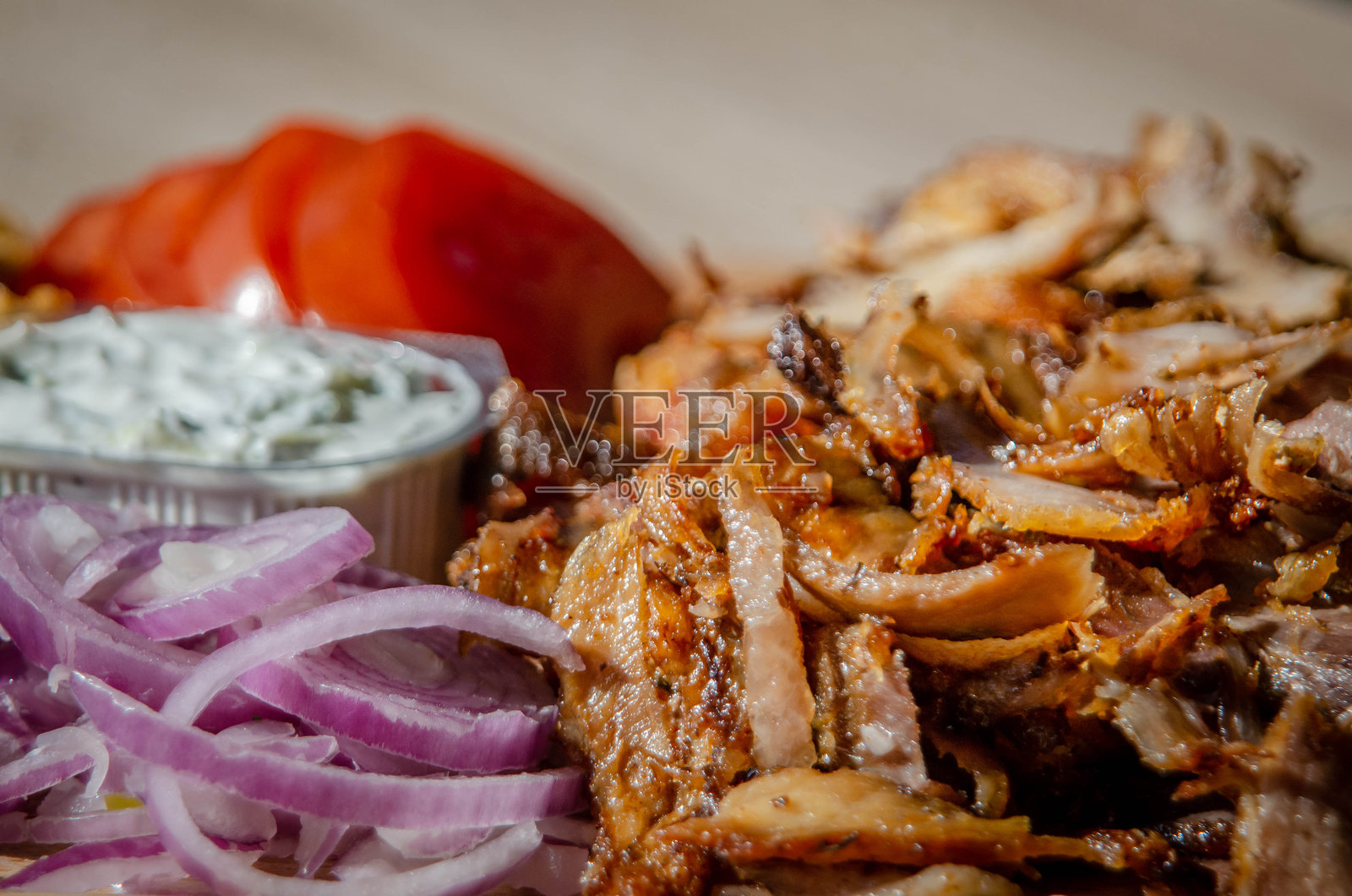 美味的希腊肉卷，配有嫩滑的肉、酥脆的薯条和新鲜的番茄，淋上浓郁的酸奶酱。它被摆放在一个质朴的木板上 - 特写镜头照片摄影图片