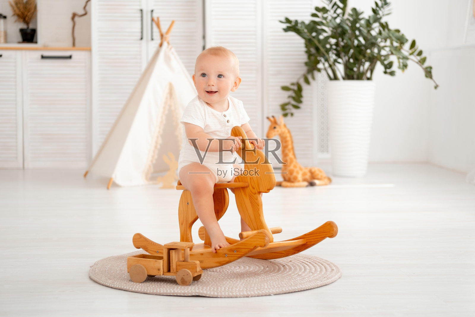 儿童房间里，婴儿在木制摇马上摇摆，一个小男孩在帐篷背景下微笑着玩耍。照片摄影图片