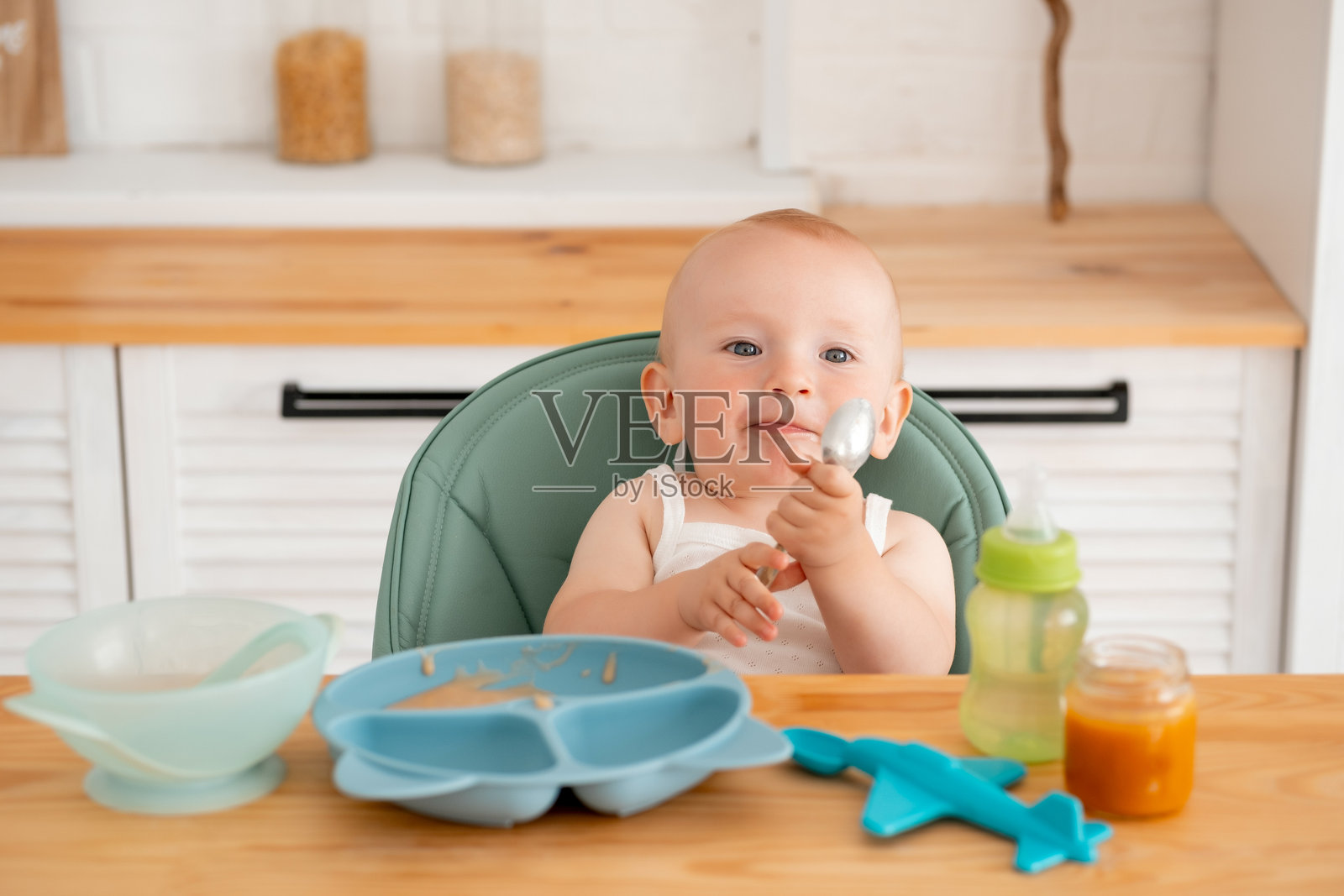 一个婴儿男孩坐在高脚椅上吃婴儿泥，一个小孩用勺子自己吃婴儿食品。照片摄影图片